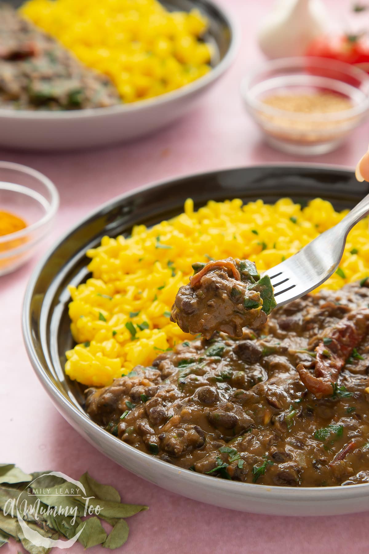 Black bean curry served to a shallow grey bowl with yellow rice. A fork reaches in.