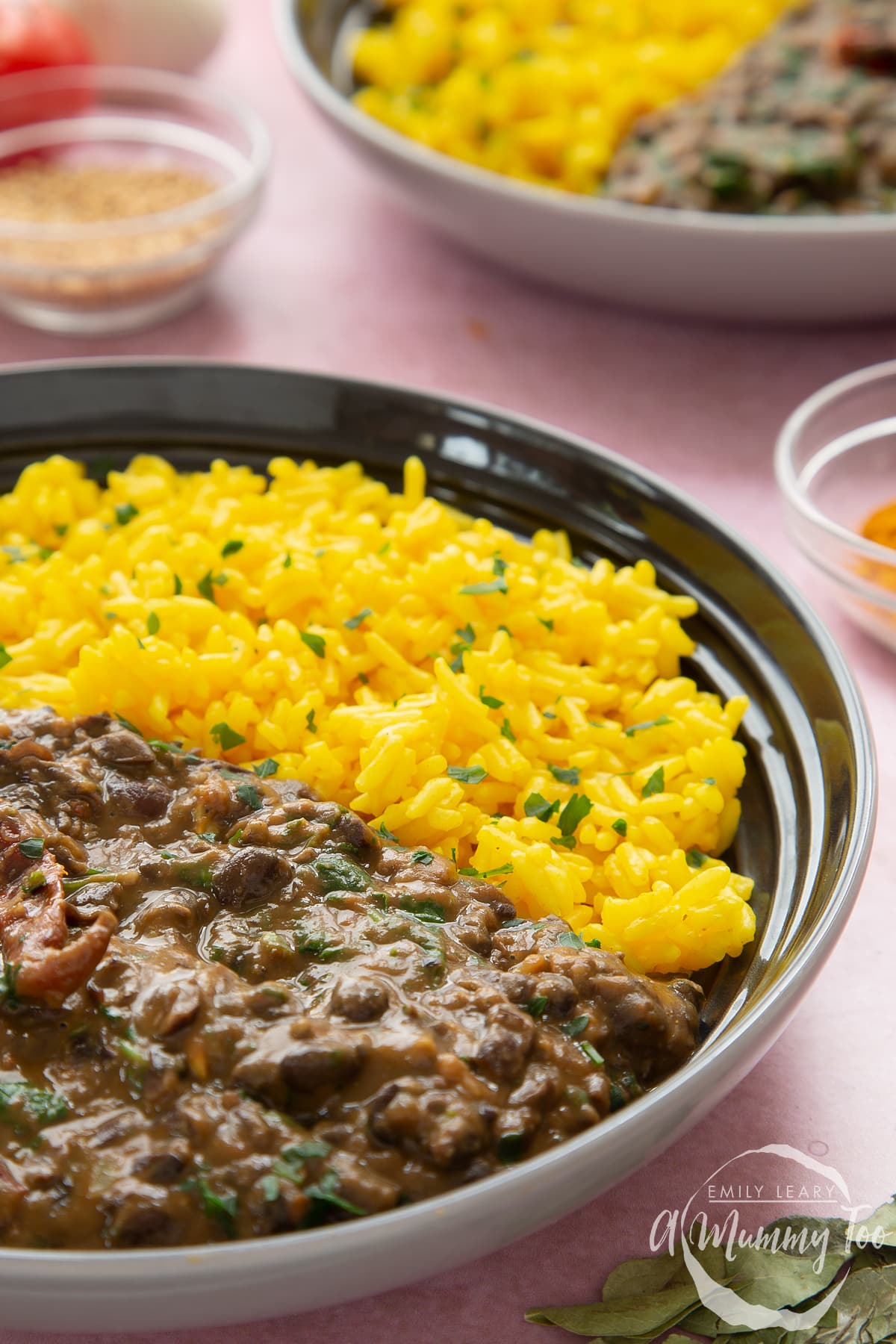 Black bean curry served to a shallow grey bowl with yellow rice scattered with chopped coriander.