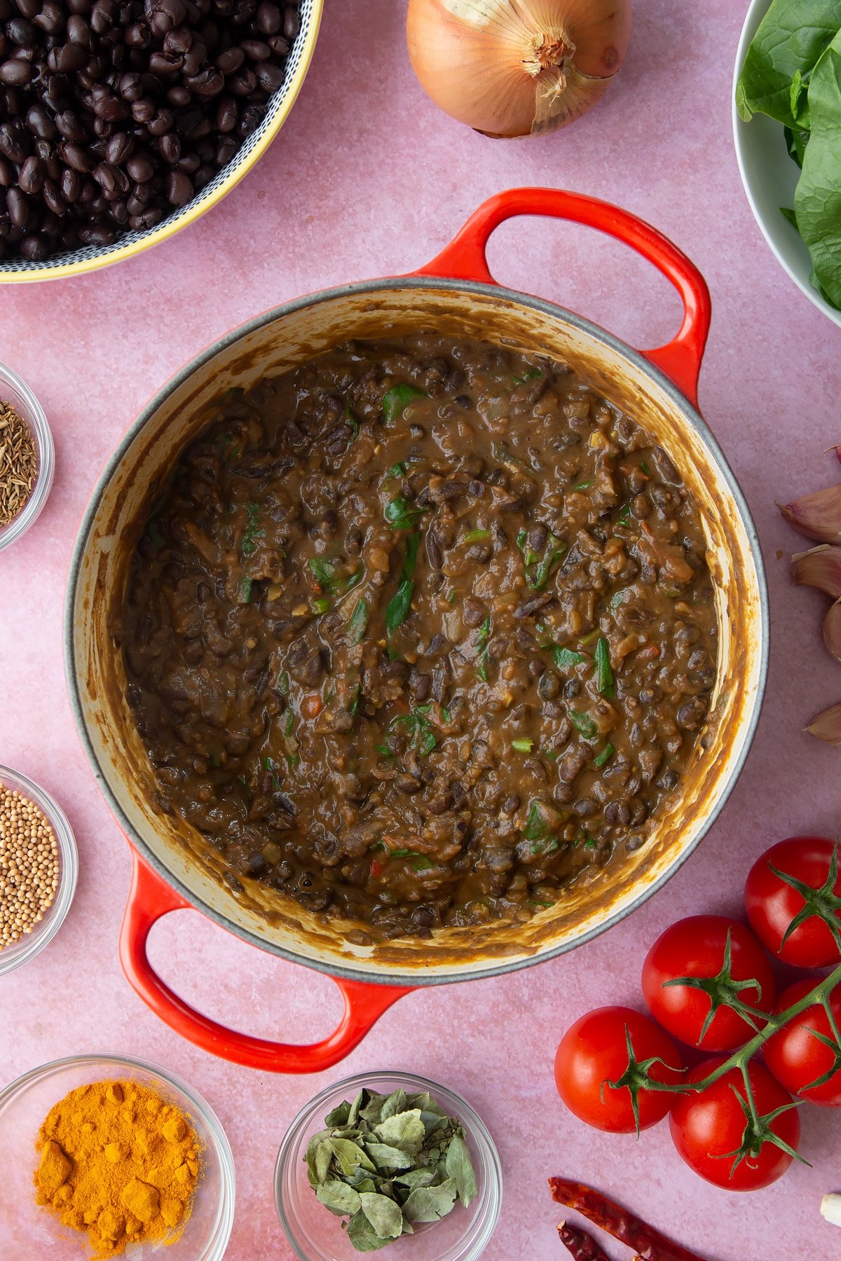 A saucepan containing black bean curry. Ingredients to make black bean curry surround the pan.