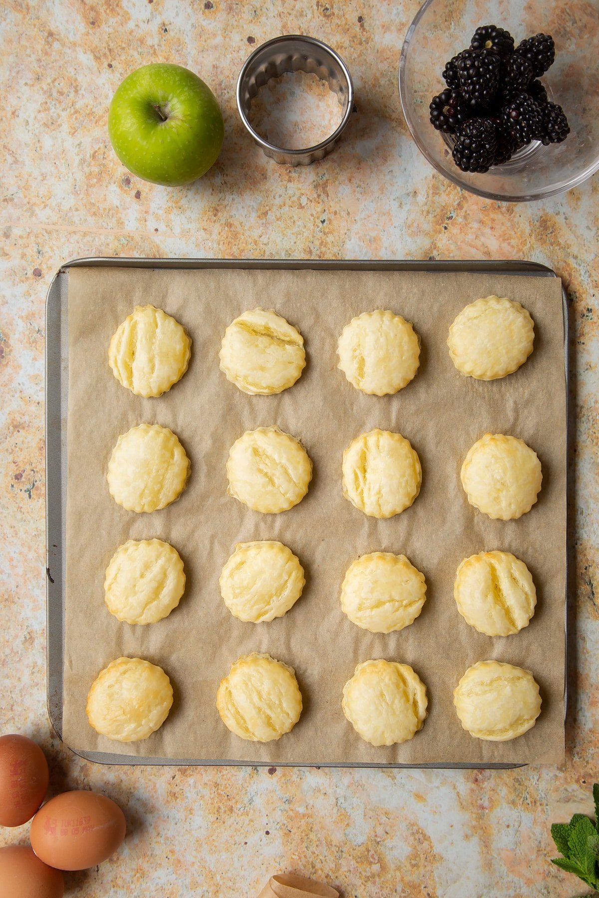 16 part-baked puff pastry discs sit on a lined baking sheet.