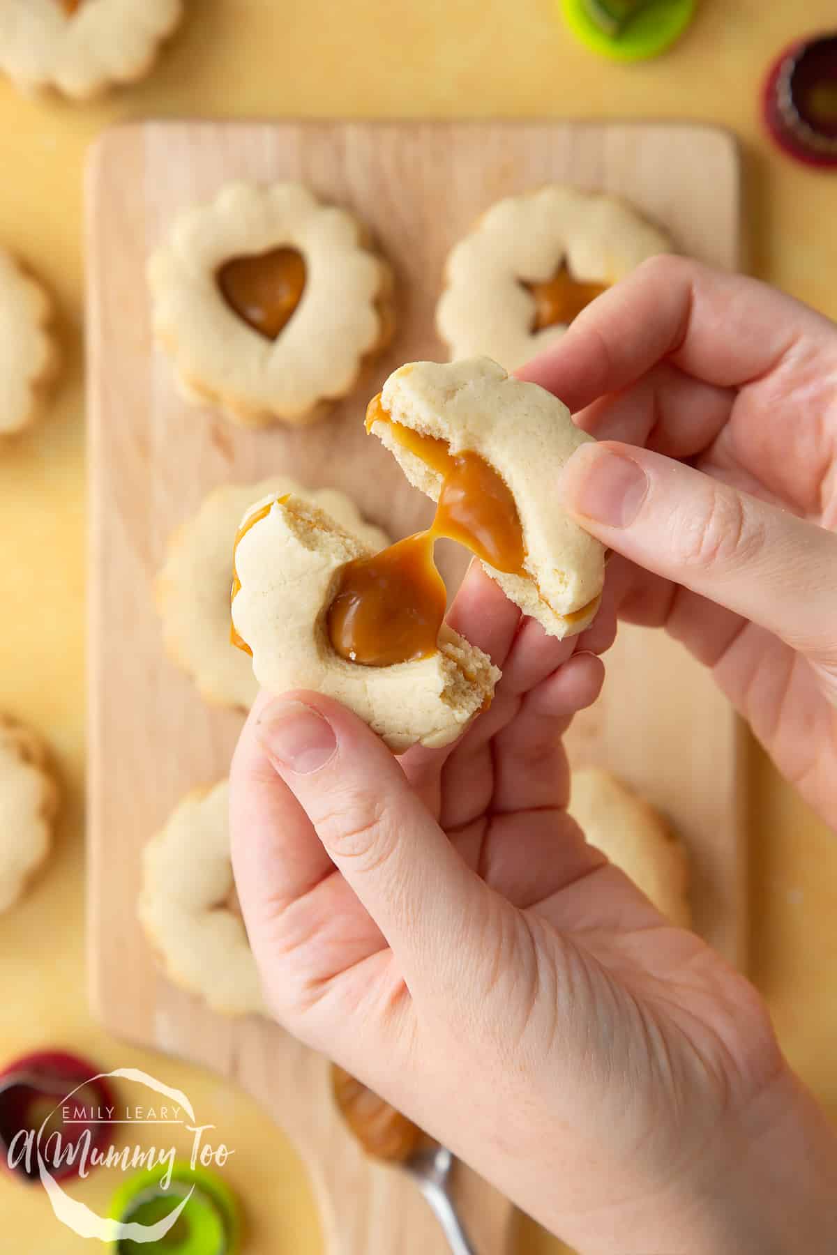 Overhead shot of a hand breaking a Caramel sandwich cookie with a mummy too logo in the lower-left corner