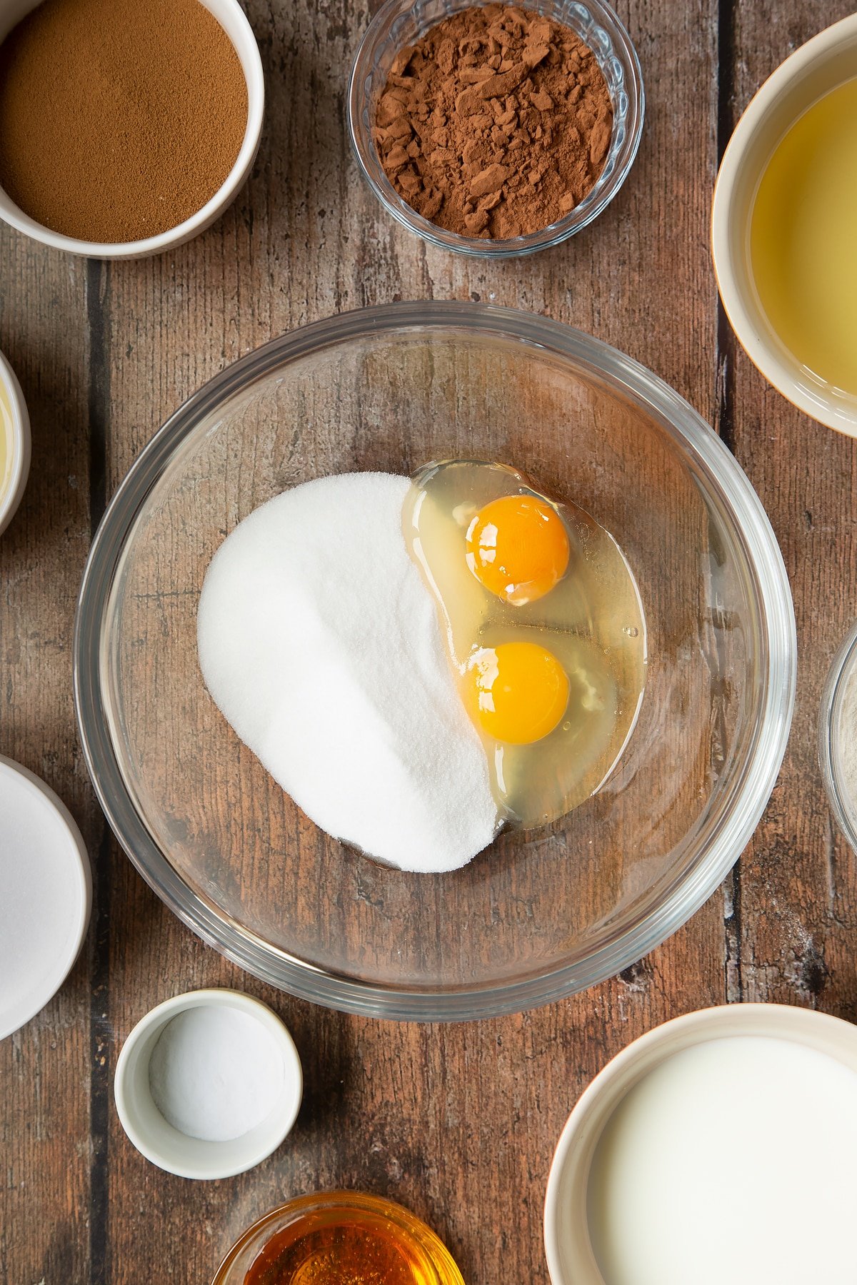 Eggs and sugar in a glass mixing bowl. Surrounding the bowl is ingredients to make dalgona coffee cake.