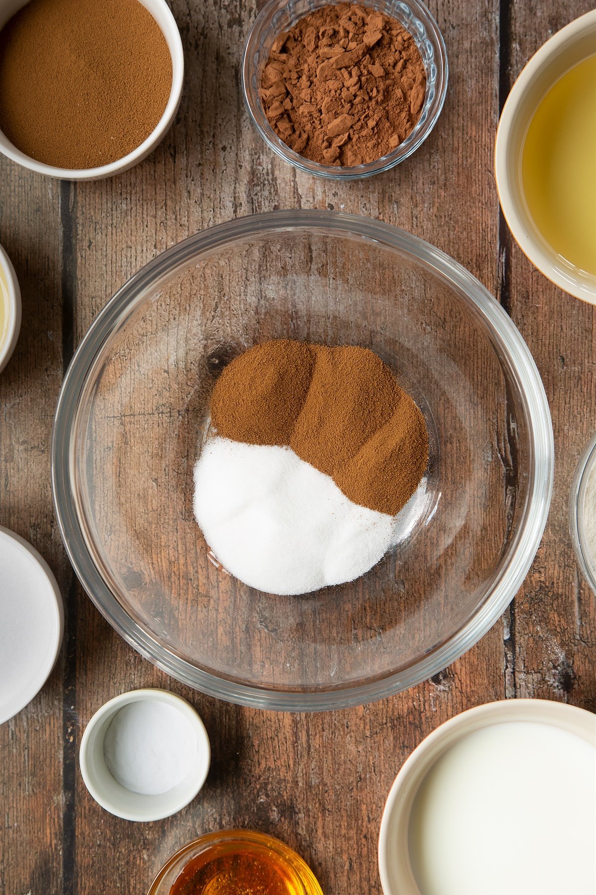 Sucre et café instantané dans un bol à mélanger en verre. Autour du bol se trouvent les ingrédients nécessaires à la préparation d'un gâteau au café dalgona.