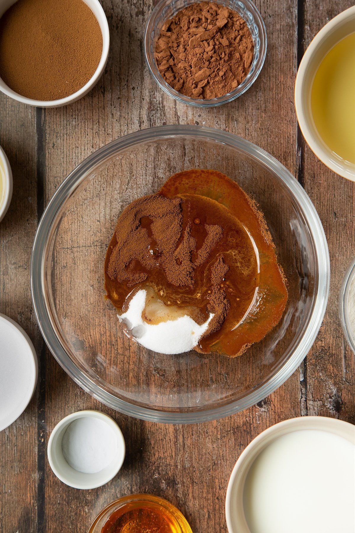 Sucre, café instantané et eau chaude dans un bol à mélanger en verre. Autour du bol se trouvent les ingrédients nécessaires à la préparation du gâteau au café dalgona.