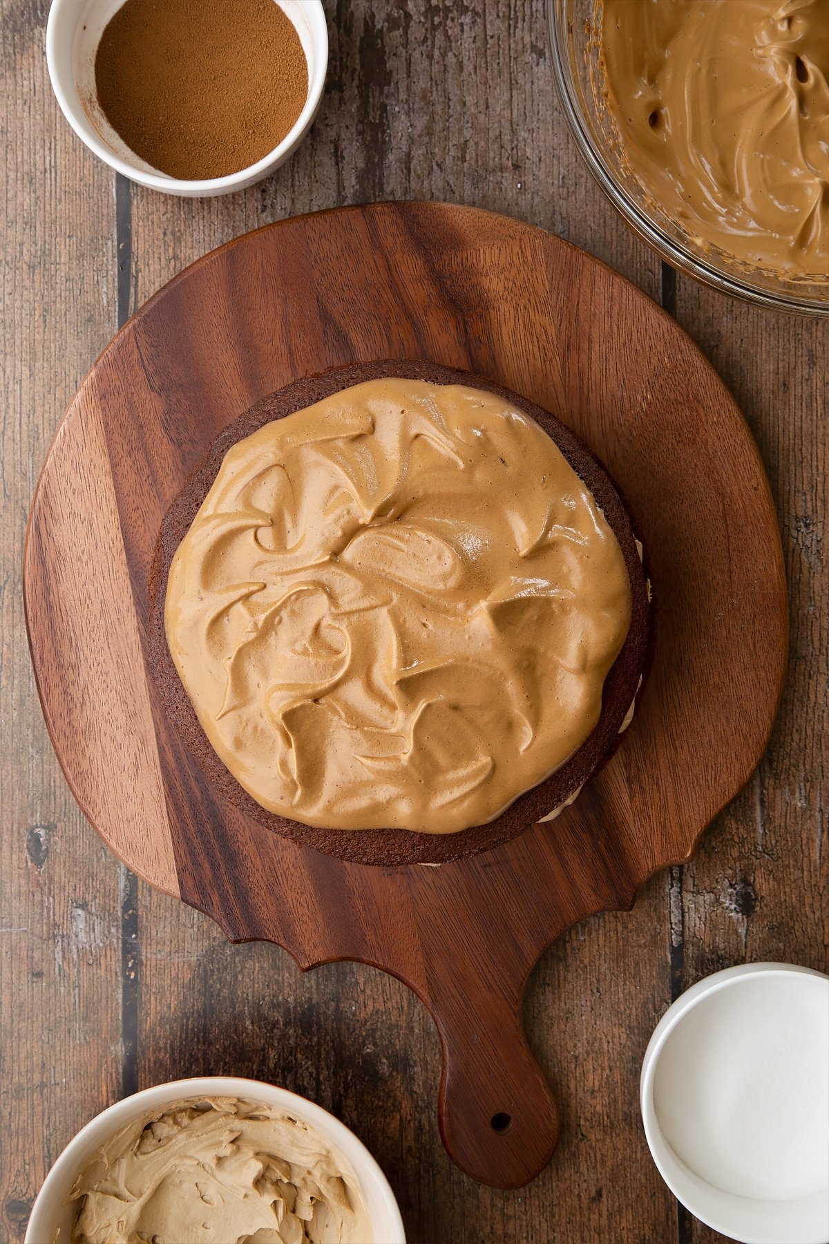 Dalgona coffee cake sponge sandwich on a wooden board. The cake is topped dalgona coffee frosting, spread into swirls and peaks.