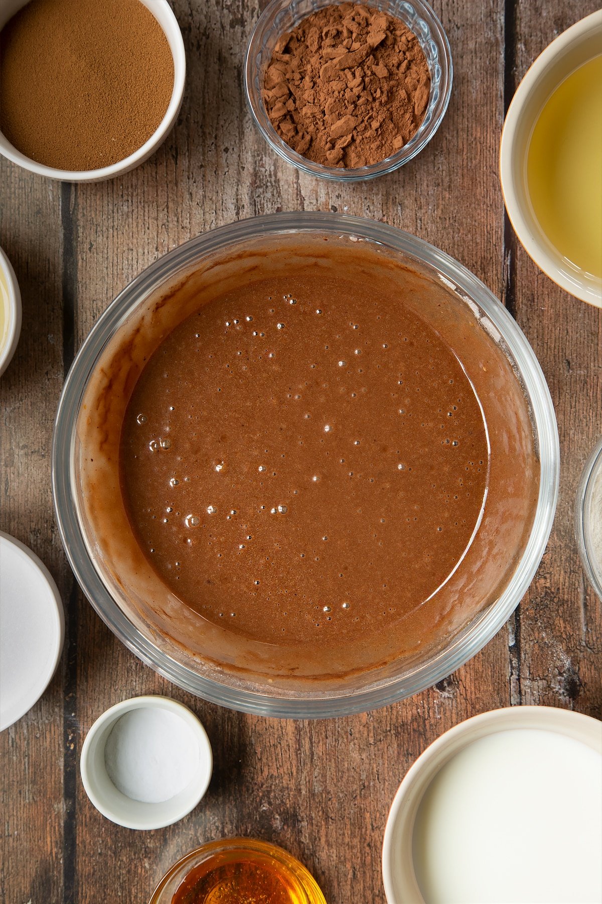 Mélange à gâteau dans un bol à mélanger en verre. Autour du bol se trouvent les ingrédients nécessaires à la préparation d'un gâteau au café dalgona.