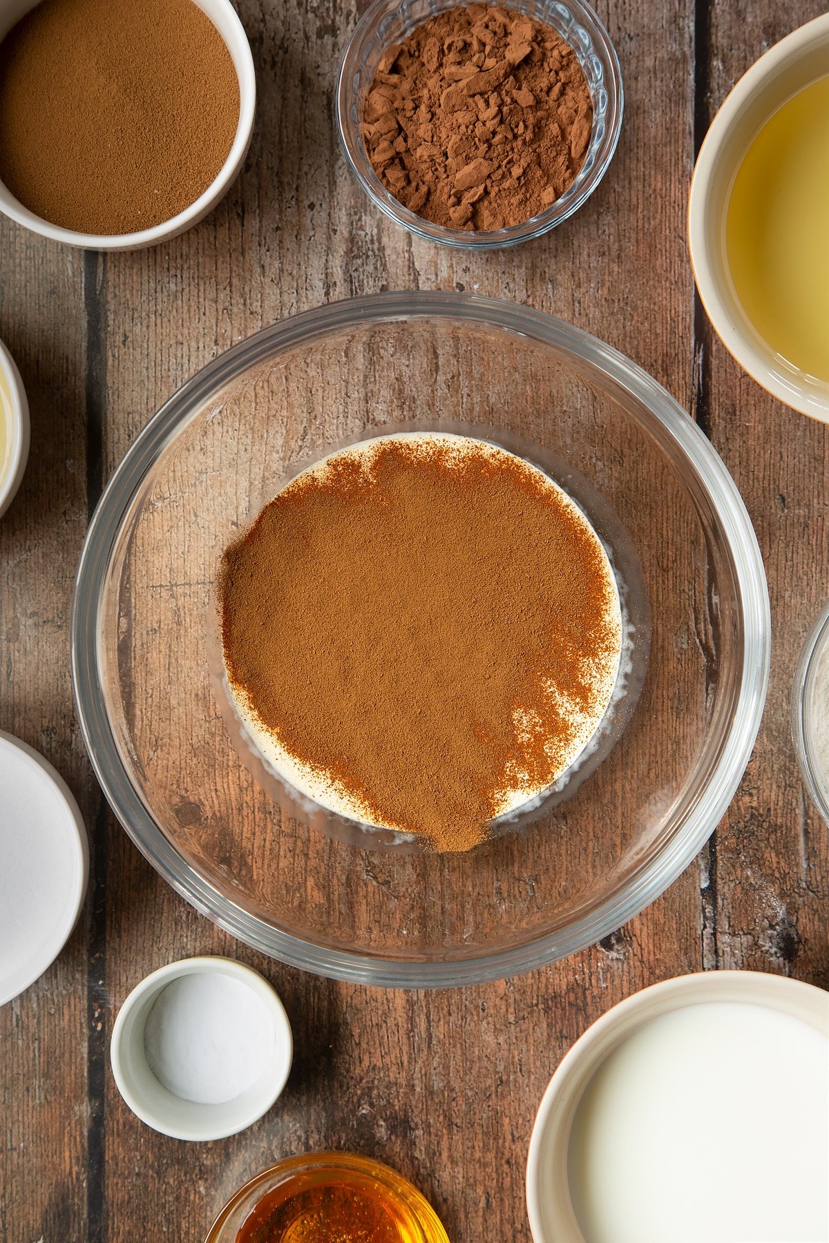 Crème double et café instantané dans un bol à mélanger en verre. Autour du bol se trouvent les ingrédients nécessaires à la préparation d'un gâteau au café dalgona.