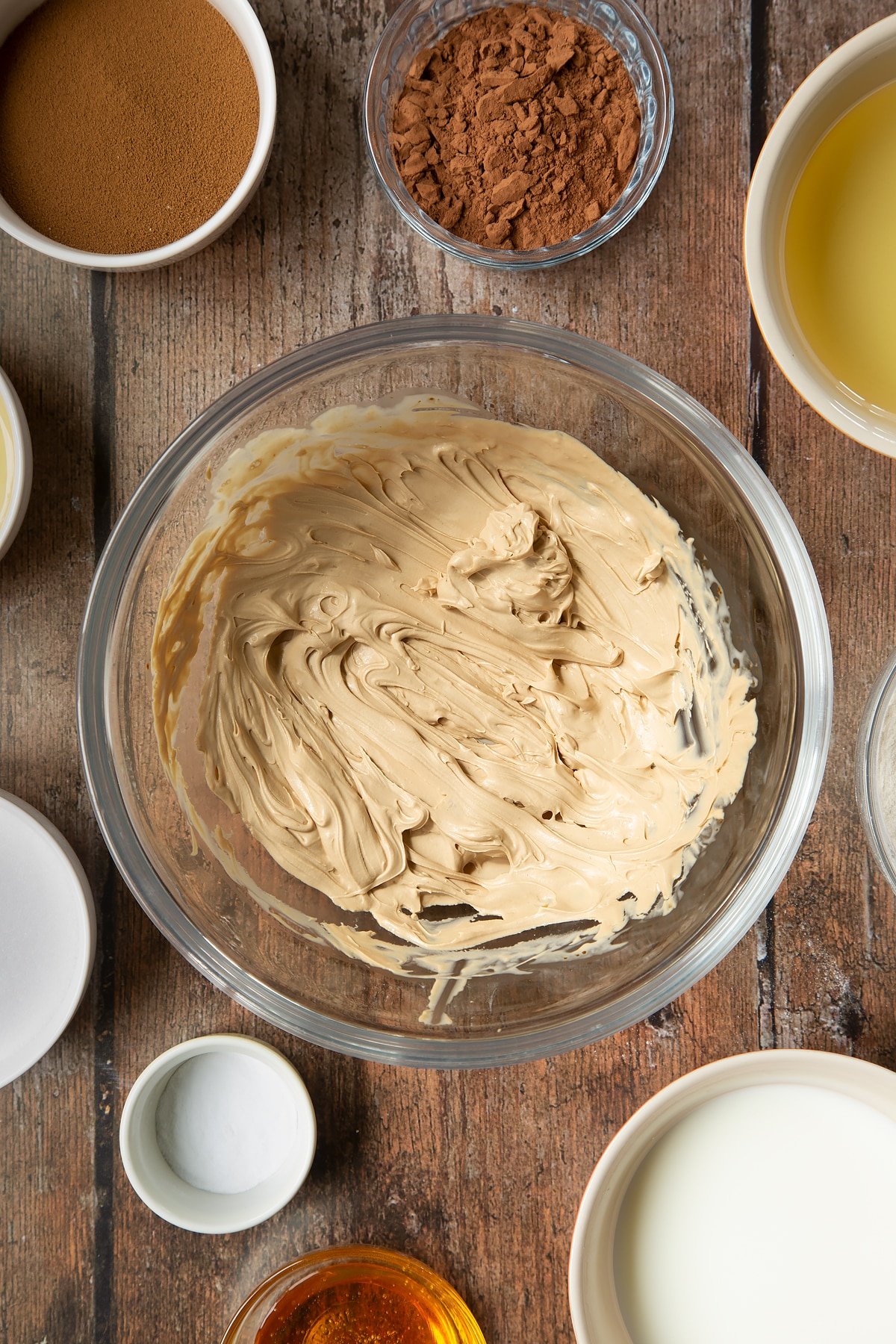 Whipped double cream and instant coffee in a glass mixing bowl. Surrounding the bowl is ingredients to make dalgona coffee cake.