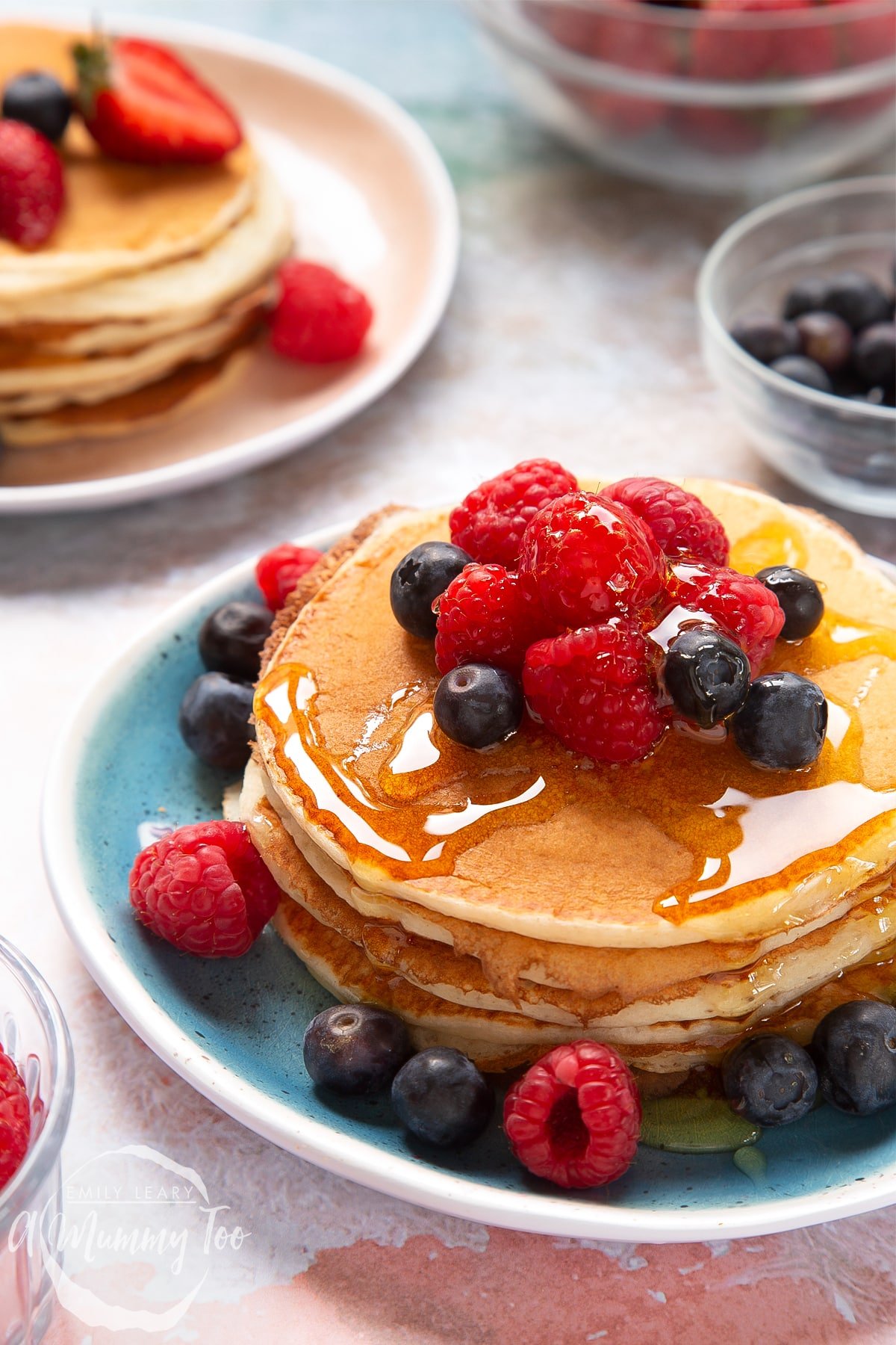 Skyr pancakes piled on a blue plate with blueberries, raspberries and honey on top.