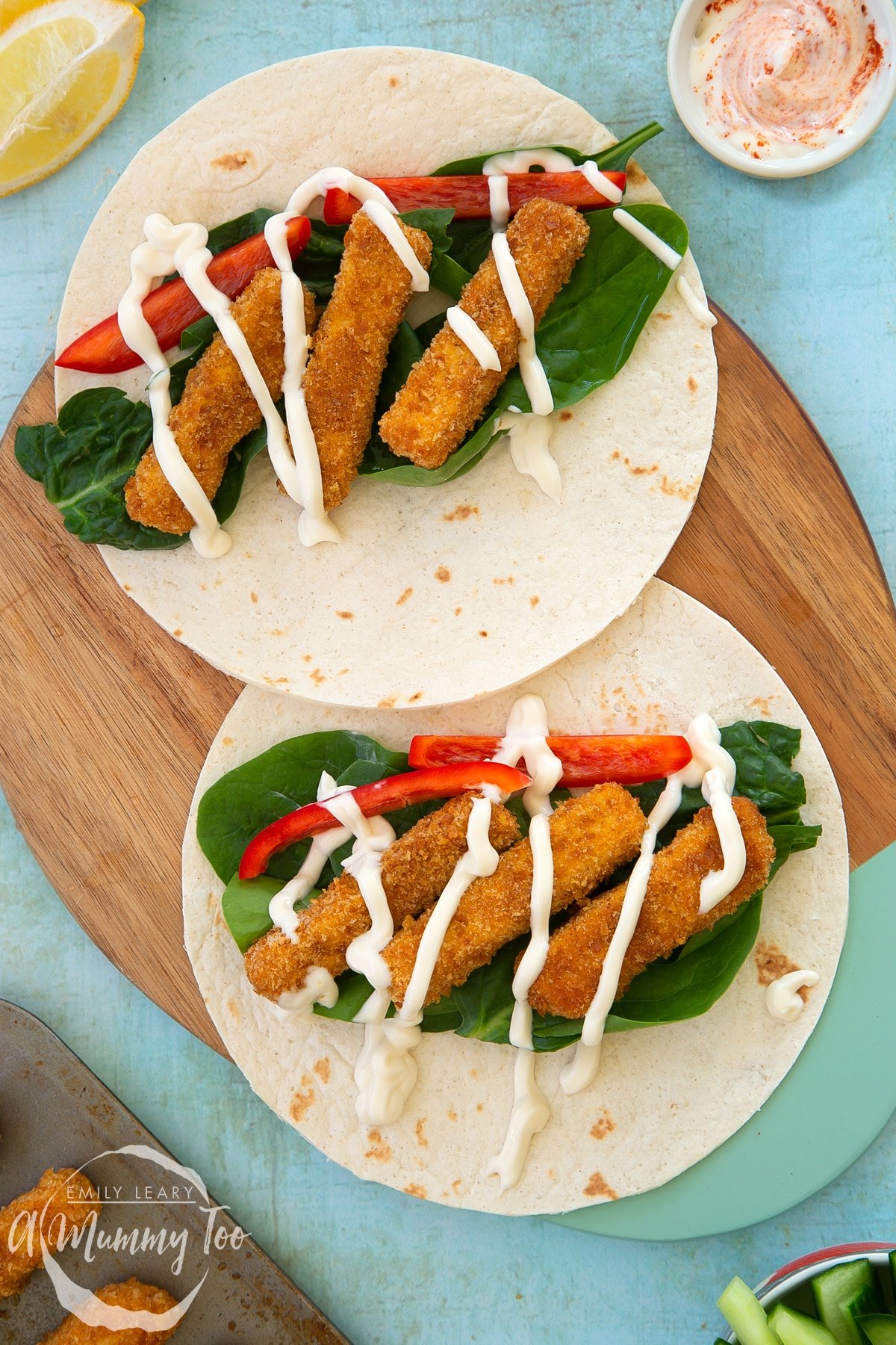 Close up of tofu fish sticks on a two flour tortillas with salad and mayo. The tortillas are placed on a wooden board.