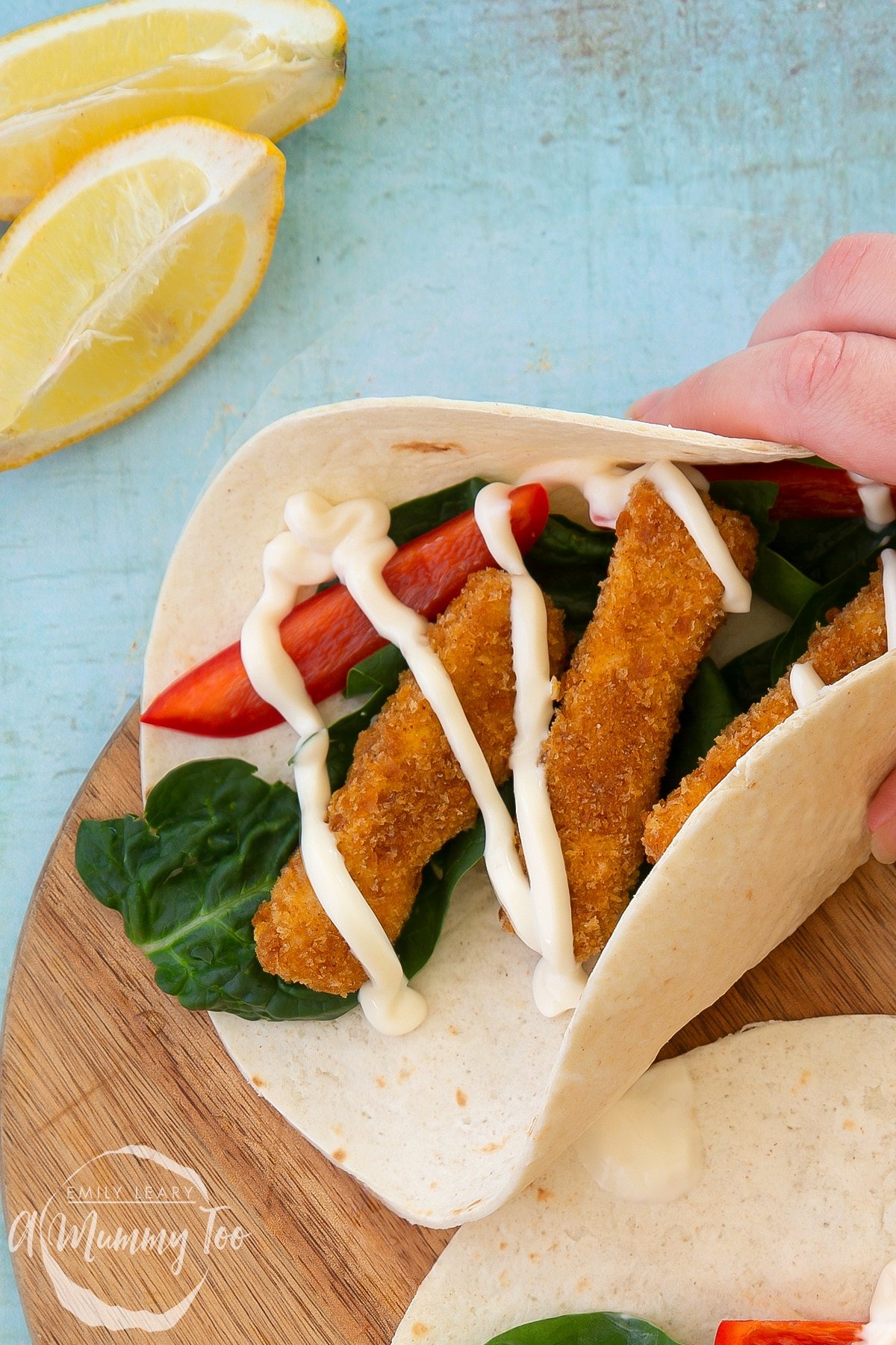 Hand picking up a flour tortilla filled with tofu fish sticks, salad and mayo.