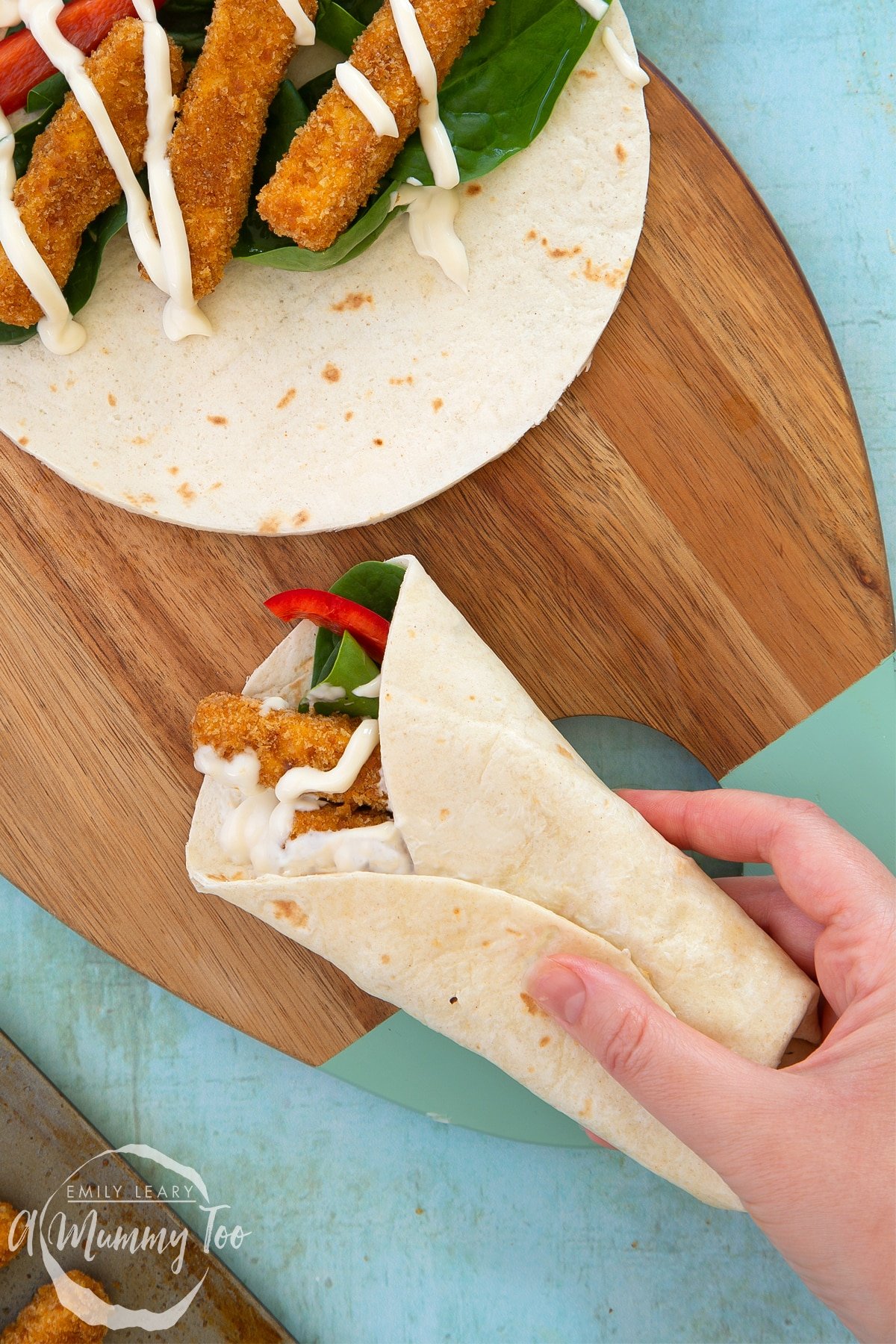 Hand holding a folded flour tortilla filled with tofu fish sticks, salad and mayo.