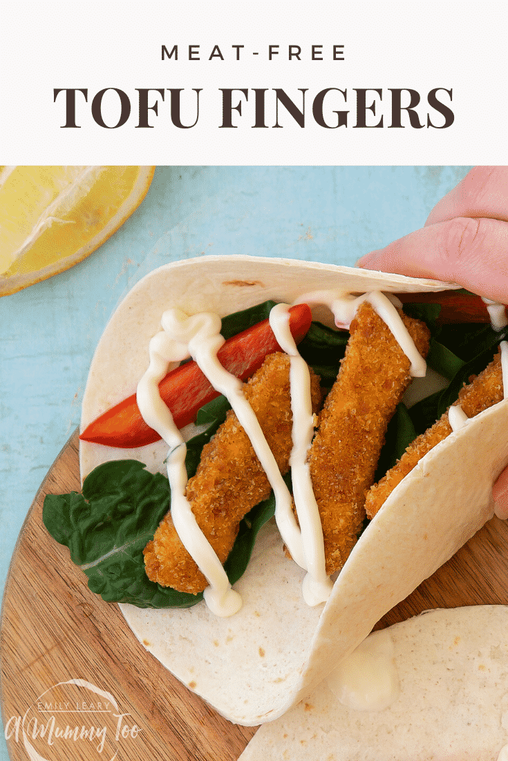 Hand holding a flour tortilla filled with tofu fish sticks, salad and mayo on a wooden board. Caption reads: meat-free tofu fish sticks.