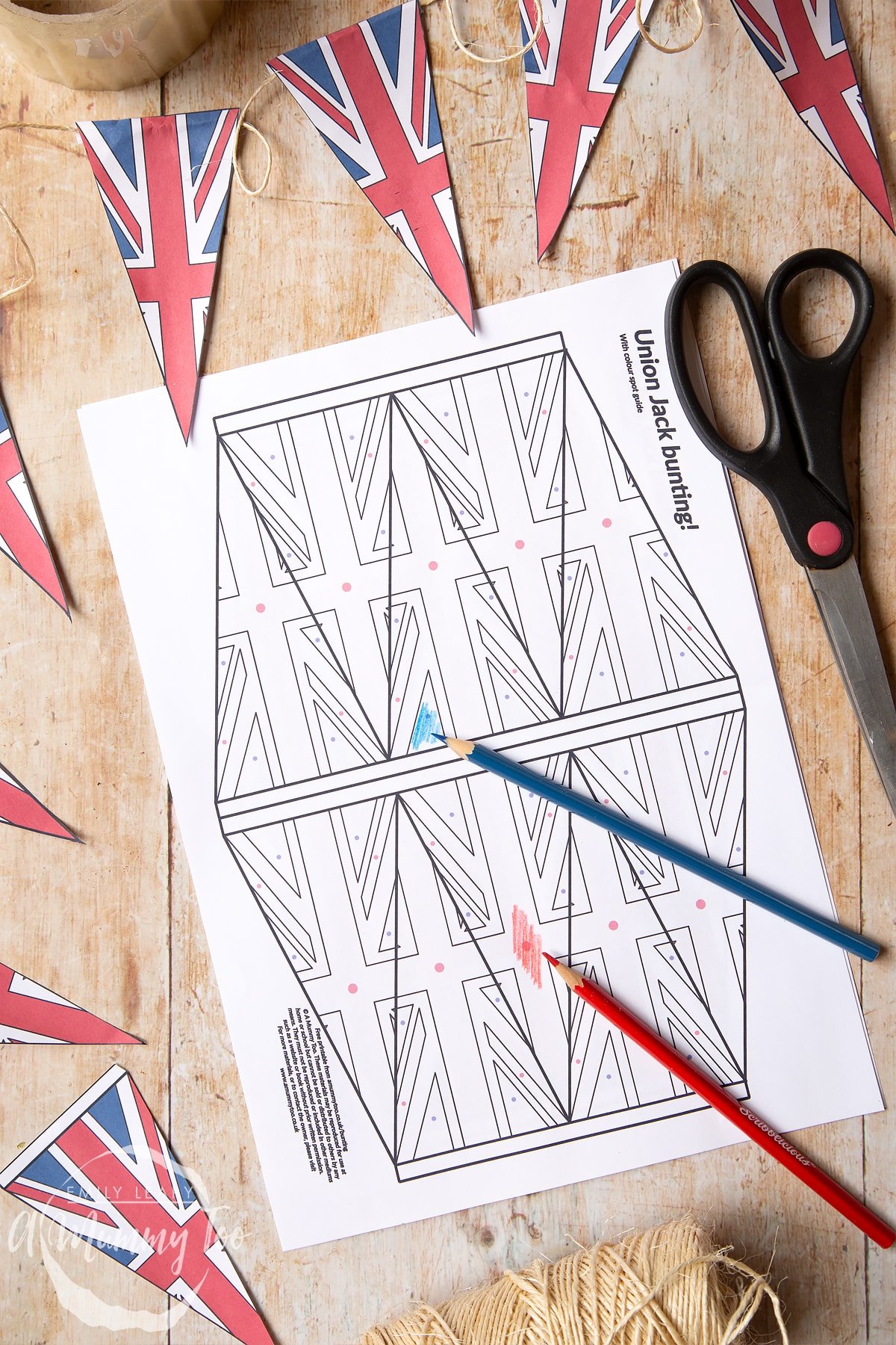 Coloured union jack bunting on string overlapping a printed black and white sheet of union jack bunting being coloured in.