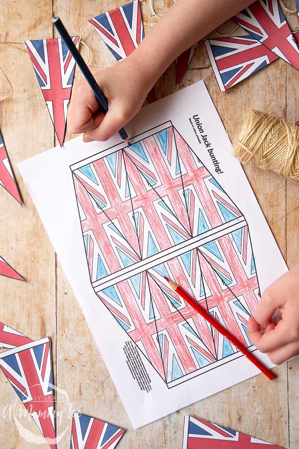 Coloured union jack bunting on string overlapping a printed black and white sheet of union jack bunting being coloured in.