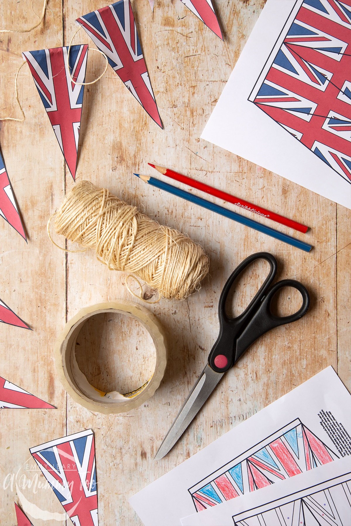 string, scissors, colouring pencils and union jack bunting printed out and laid out on a wooden backdrop.