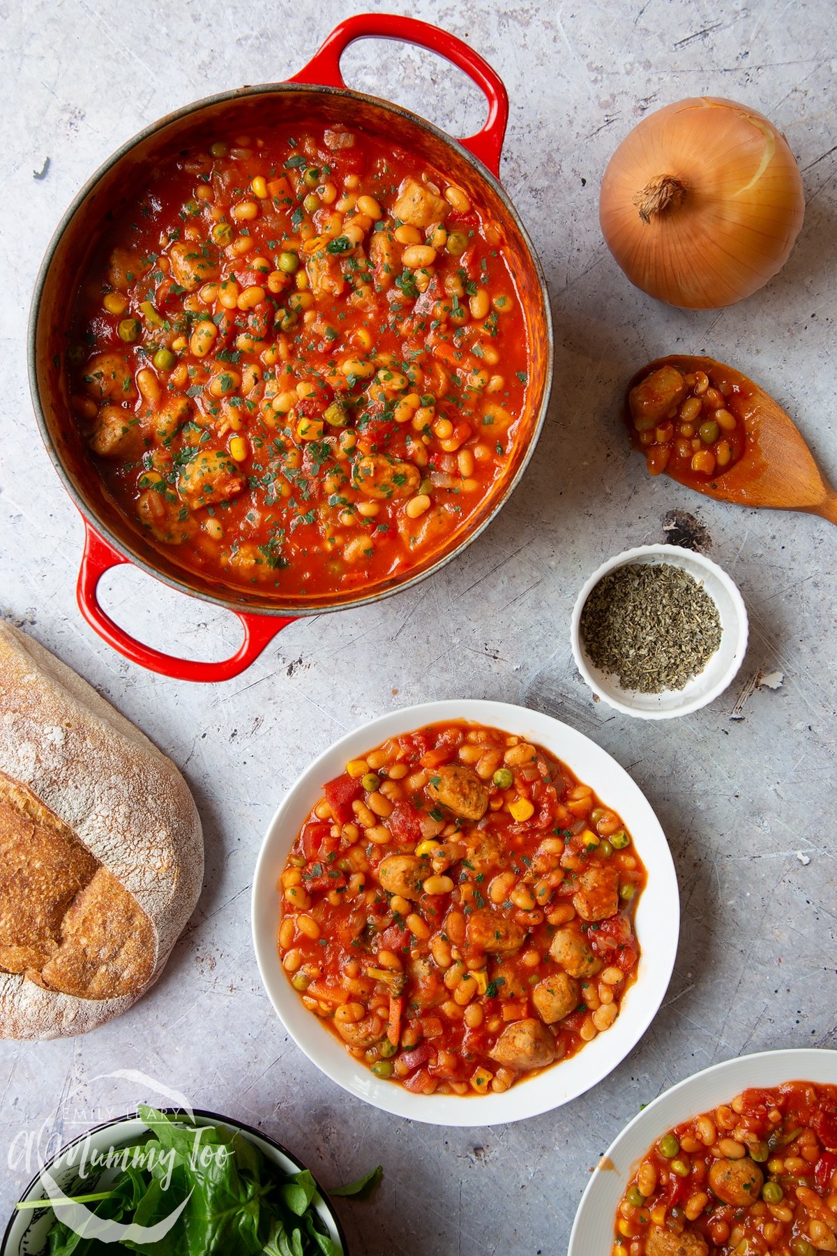 Veggie sausage and bean casserole served into a shallow white bowl. A large pot of casserole is also shown alongside a large loaf of crusty bread.