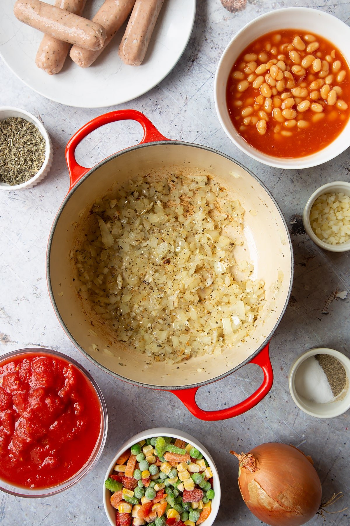 Fried onions in a large pot. Ingredients to make veggie sausage and bean casserole surround the pot.