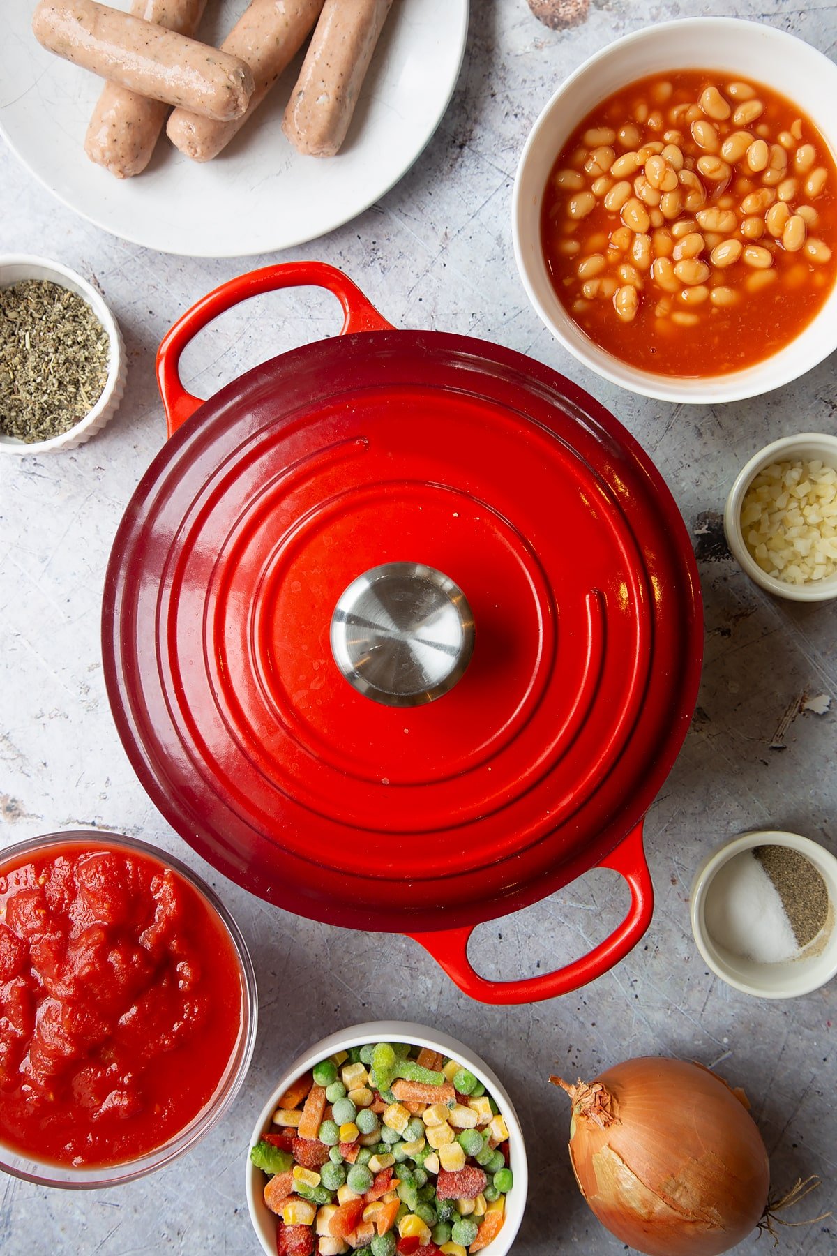 Large pot with red lid on. Ingredients to make veggie sausage and bean casserole surround the pot.