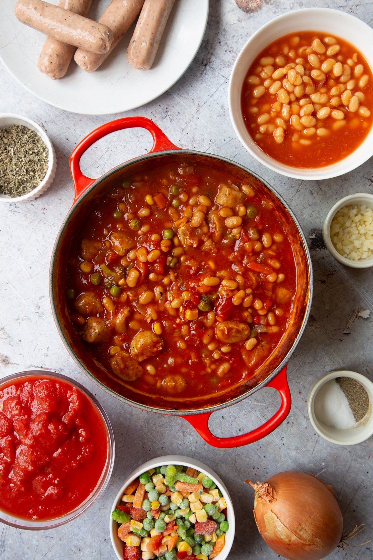 Vegetarian sausage and bean casserole in a large pot. Ingredients to make veggie sausage and bean casserole surround the pot.