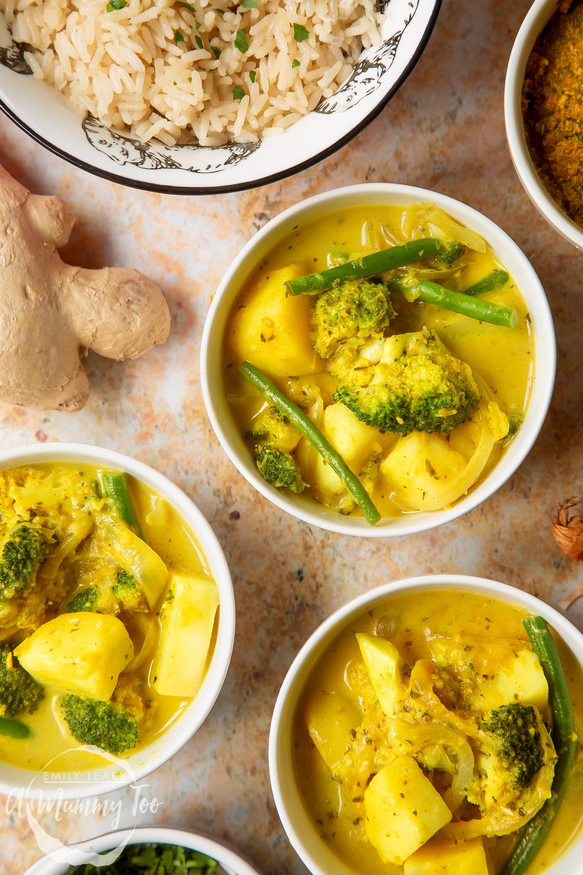 Vegetarian yellow curry with broccoli, potato and green beans, served to small white bowls. A bowl of rice is also shown.