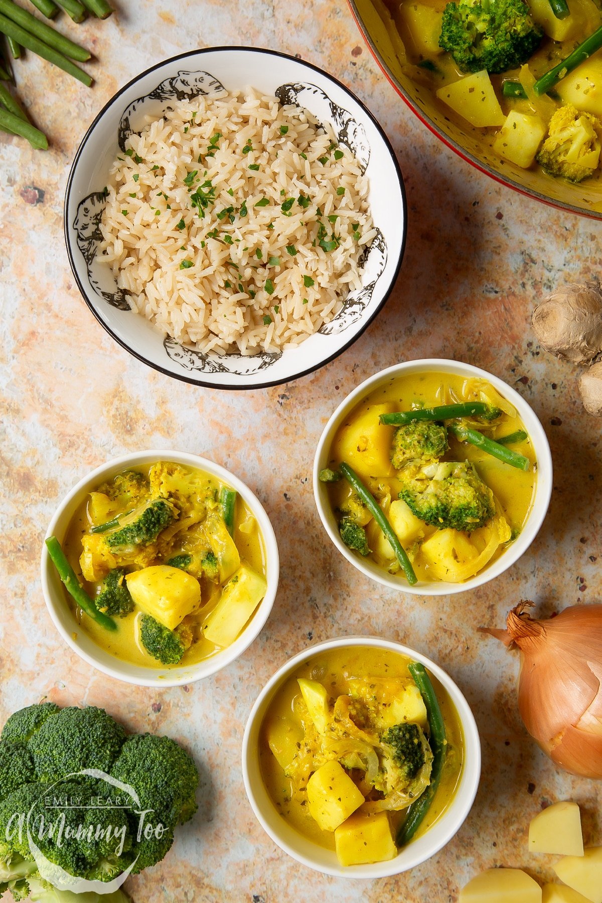 Vegetarian yellow curry with broccoli, potato and green beans, served to small white bowls. A bowl of rice is also shown alongside some ingredients. 