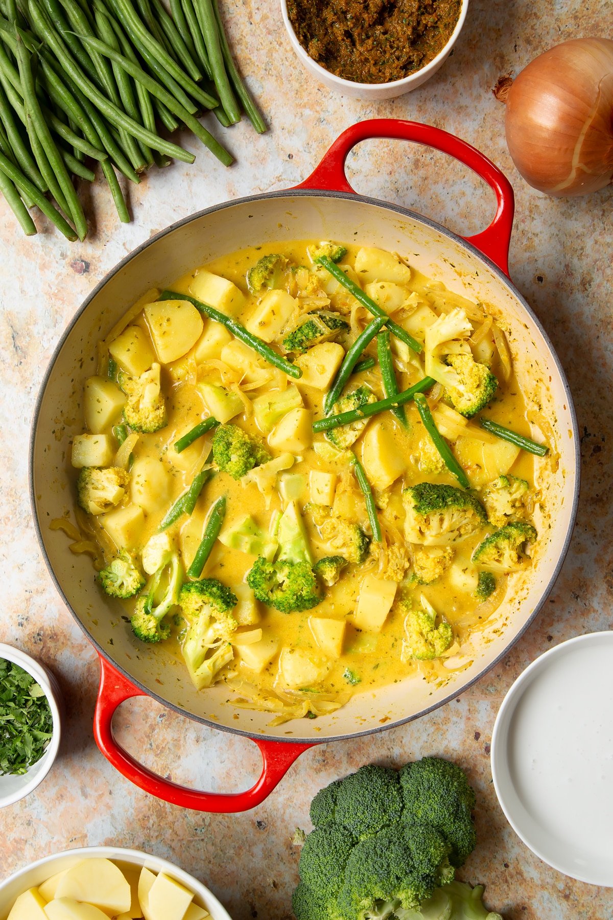 Vegetarian yellow curry in a large pan. Ingredients to make the curry surround the pan.