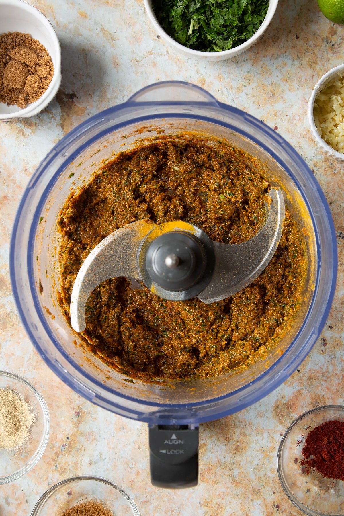 Yellow curry paste in a food processor bowl. Ingredients to make vegetarian yellow curry surround the bowl.