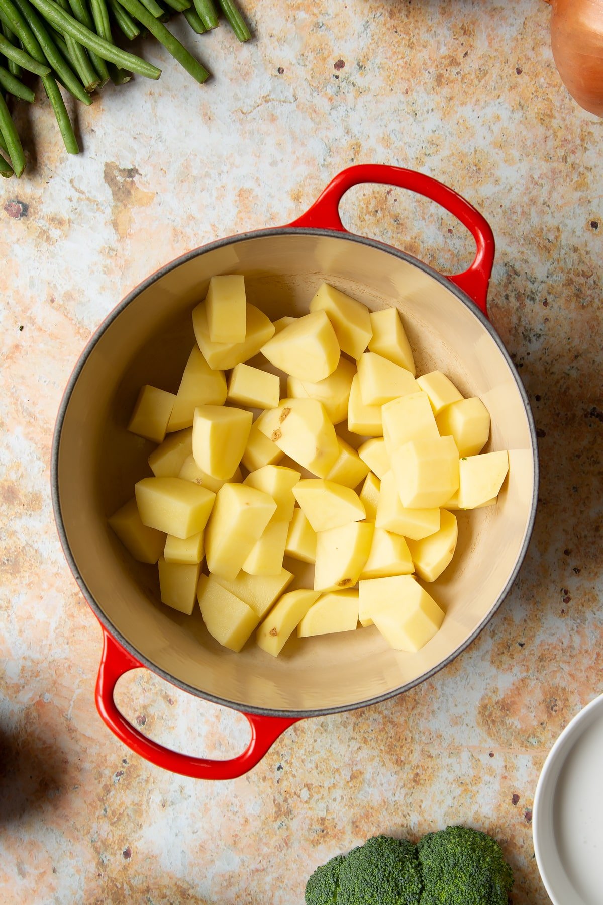 Peeled and chopped potatoes in a saucepan. Ingredients to make vegetarian yellow curry surround the pan.