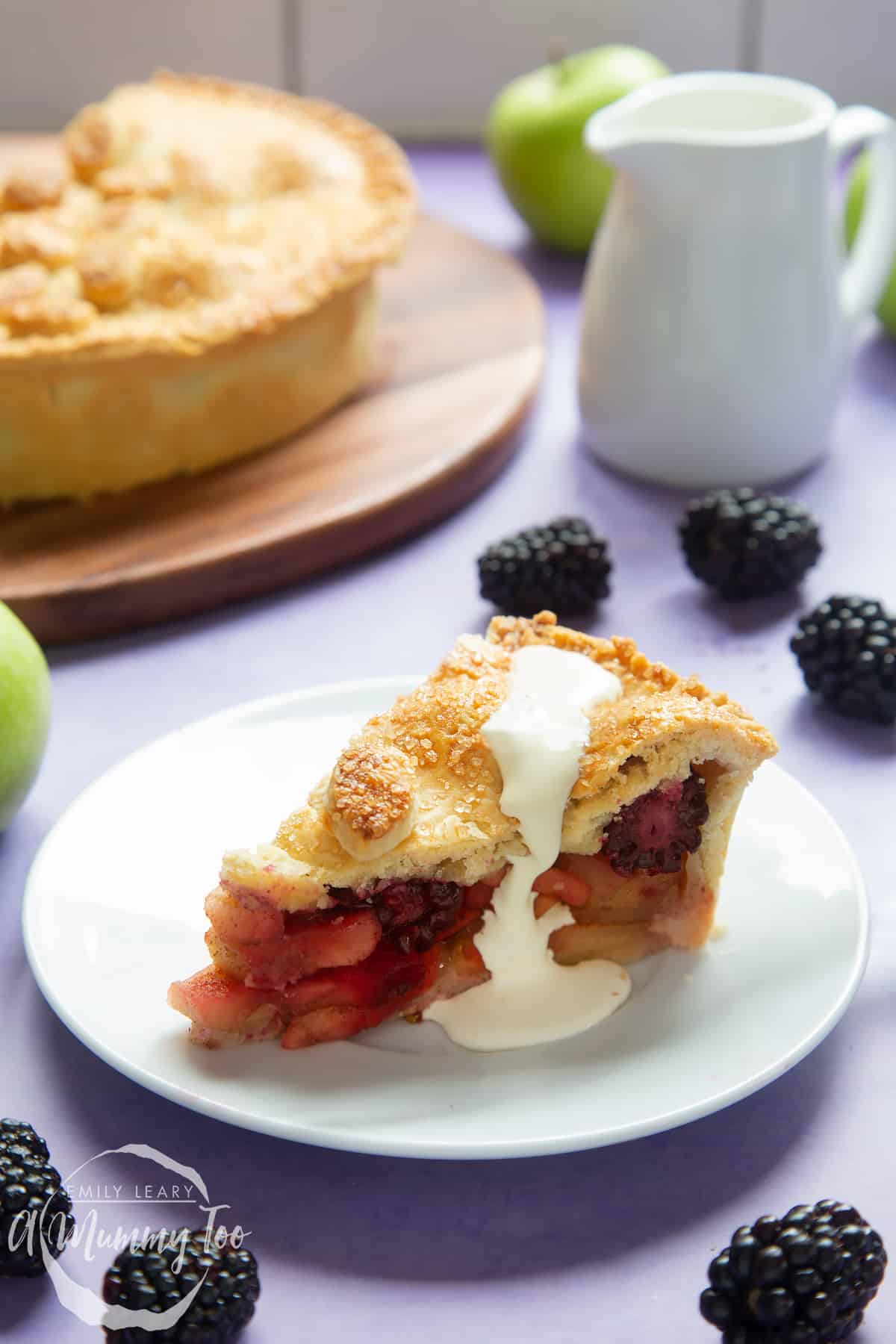 A slice of apple and blackberry pie on a white plate. Cream has been poured on top.