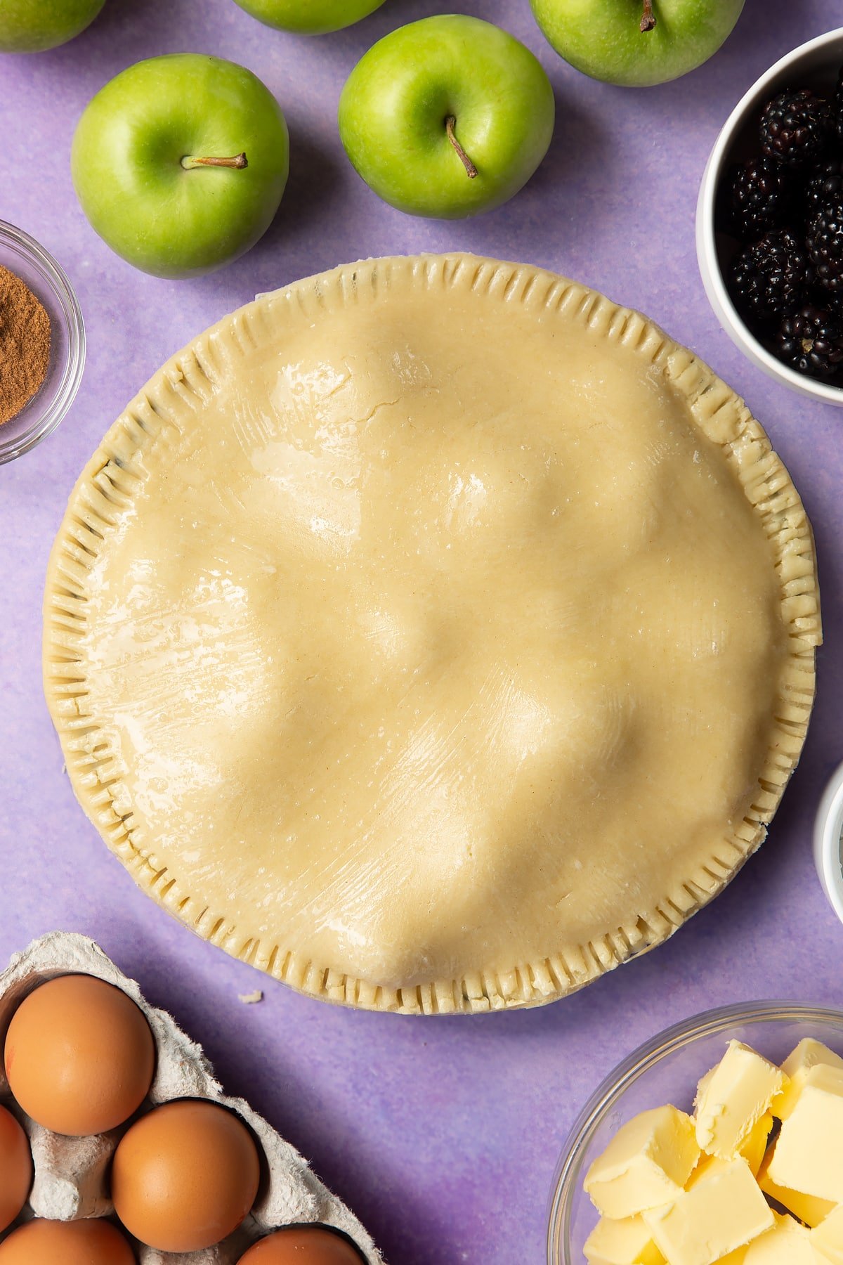 A raw apple and blackberry pie in a tin. The top has been brushed with egg white.