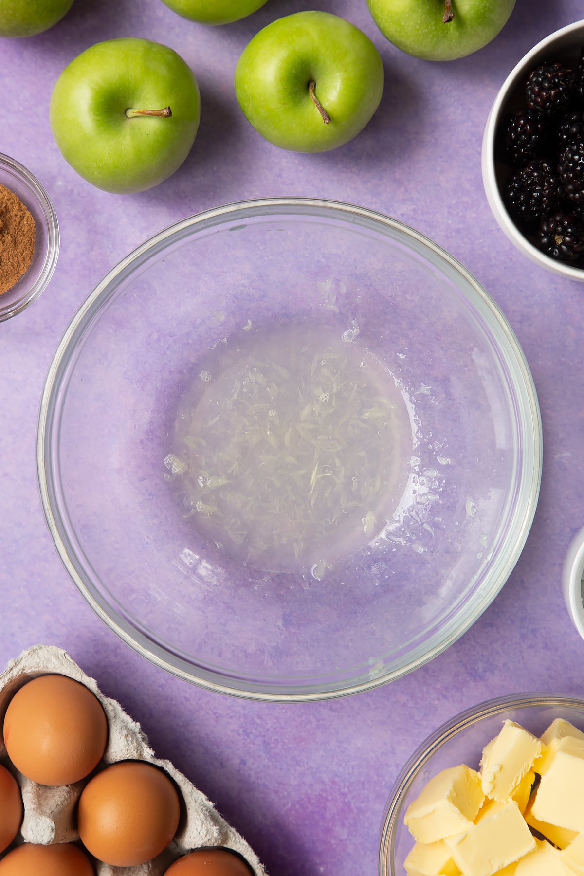 Lemon juice in a glass mixing bowl. Ingredients to make apple and blackberry pie surround the bowl.