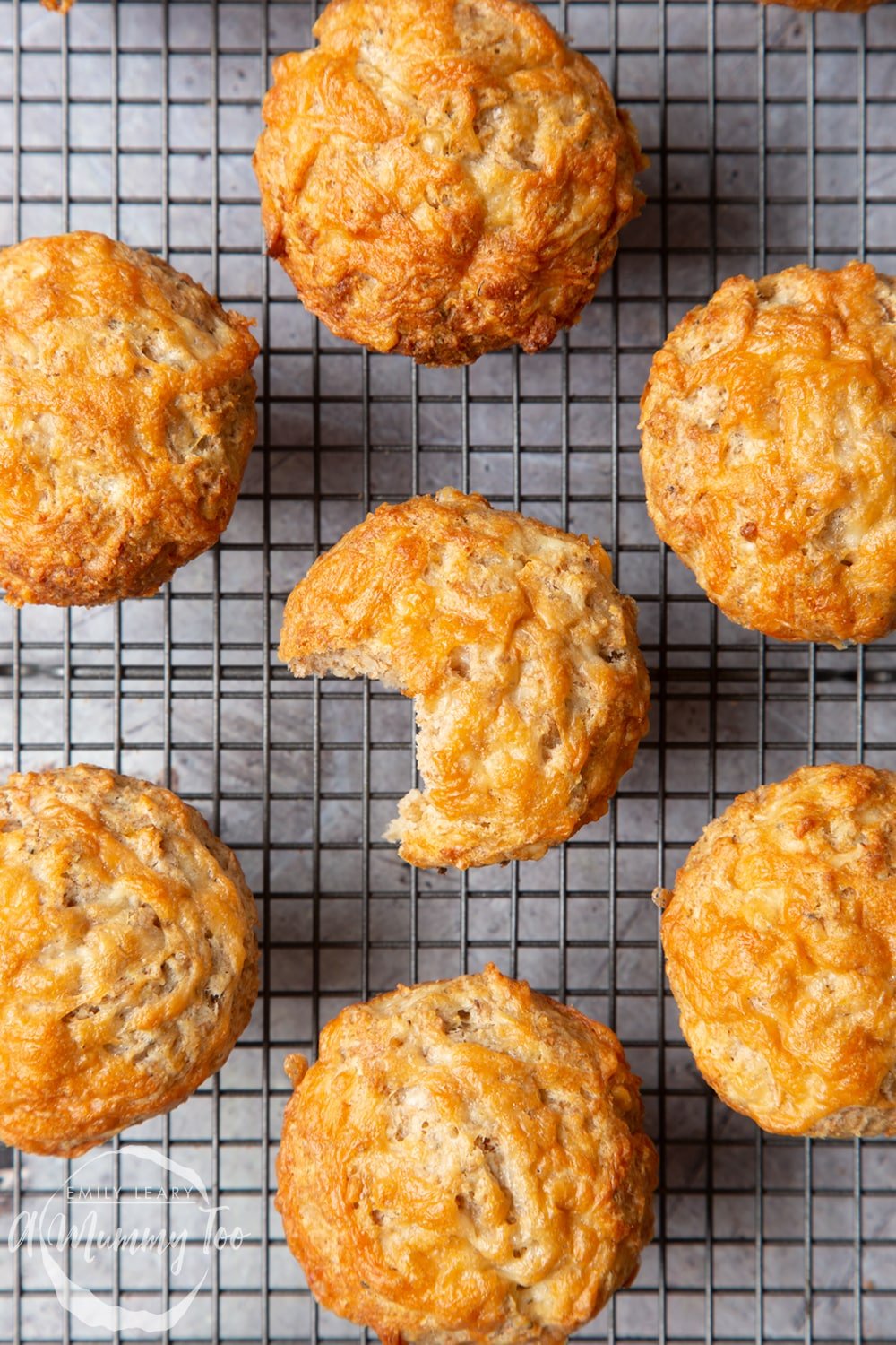 Easy cheese muffins cooling on a wire rack. One has a bite taken out of it.