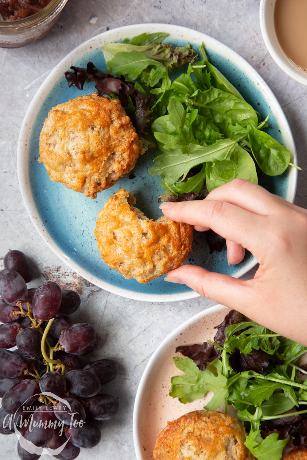 Easy cheese muffins served to two plates with leafy salad. One has a bite out of it and a hand reaches to take it.