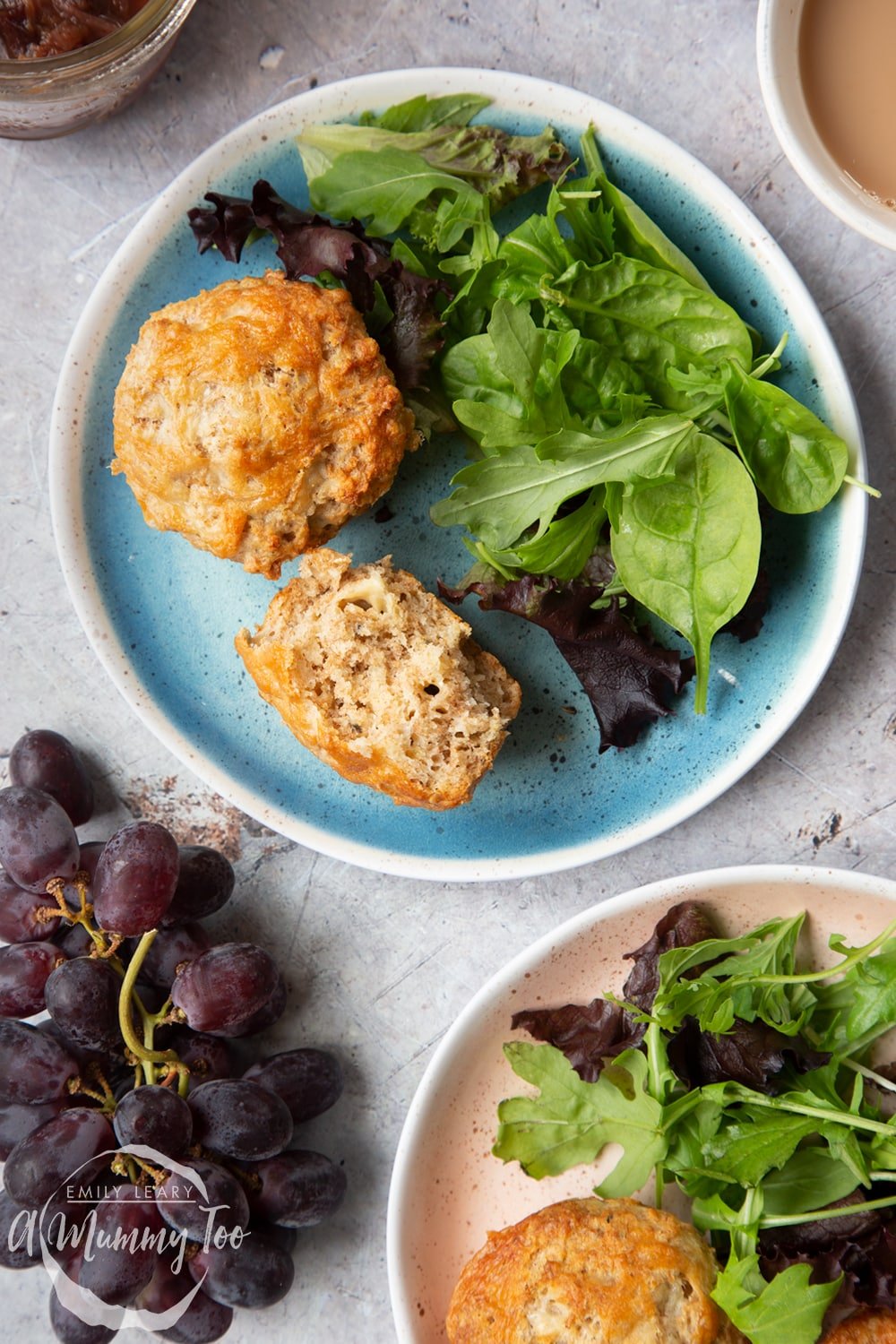 Easy cheese muffins served to two plates with leafy salad. One is broken open and turned on its side to show the cheesy crumb inside.