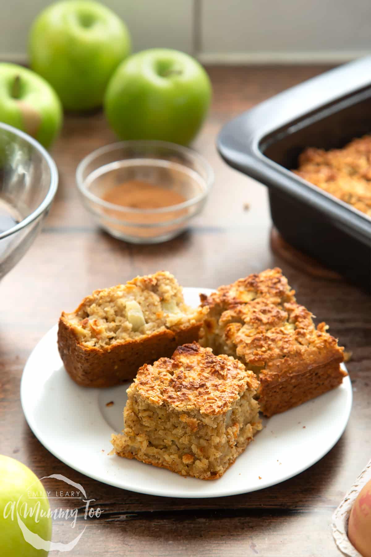 Three porridge squares on a white plate. Apples are shown in the background.