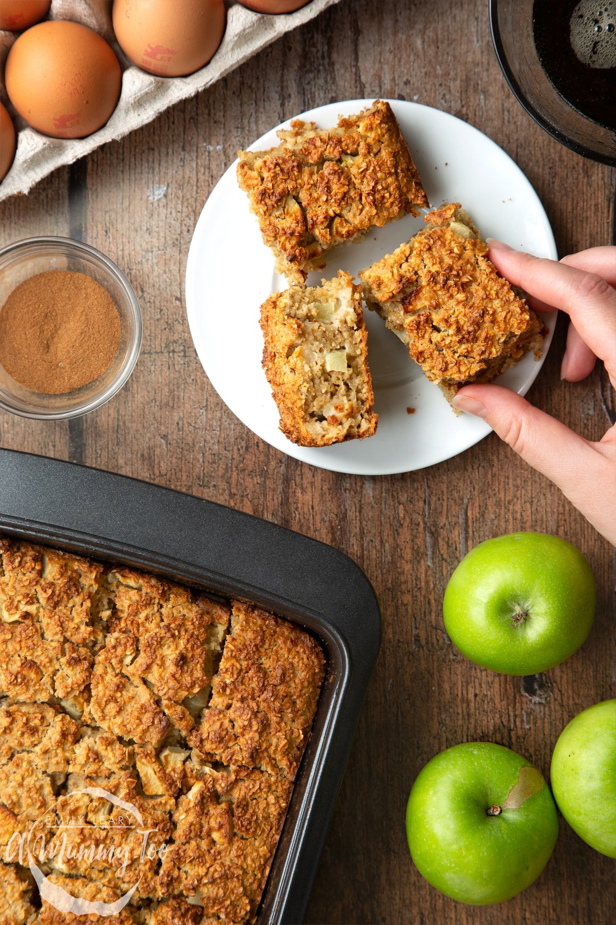 Three porridge squares on a white plate. A hand reaches for one. More of the porridge squares is shown in a baking tray.