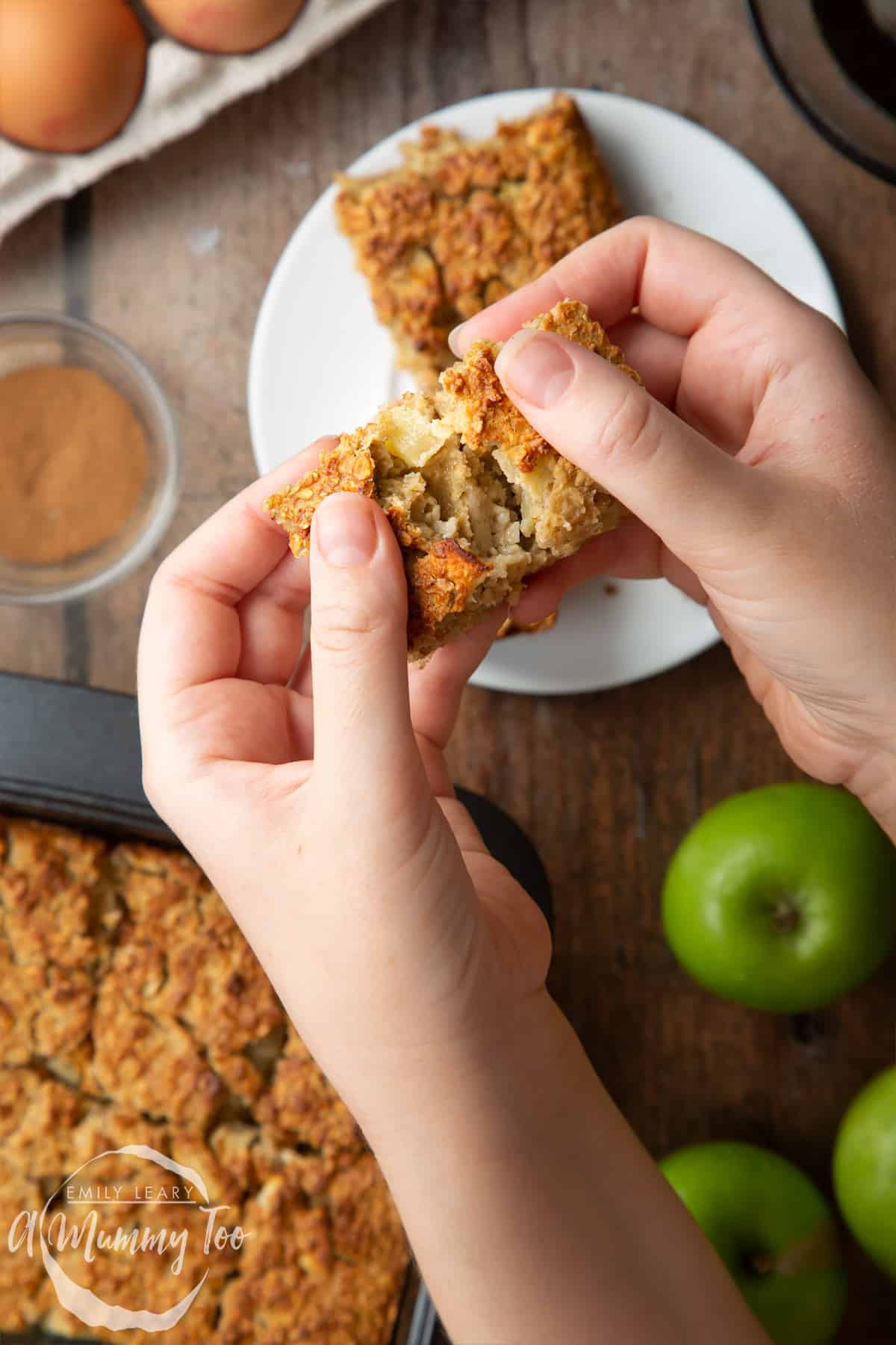 Hands breaking open a porridge square. Apples and more of the porridge squares are shown in the background.