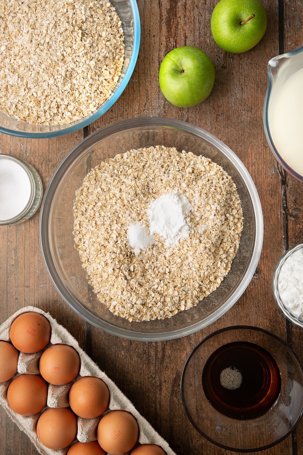 Oats, baking powder and salt in a glass mixing bowl. Ingredients to make porridge squares surround the bowl.