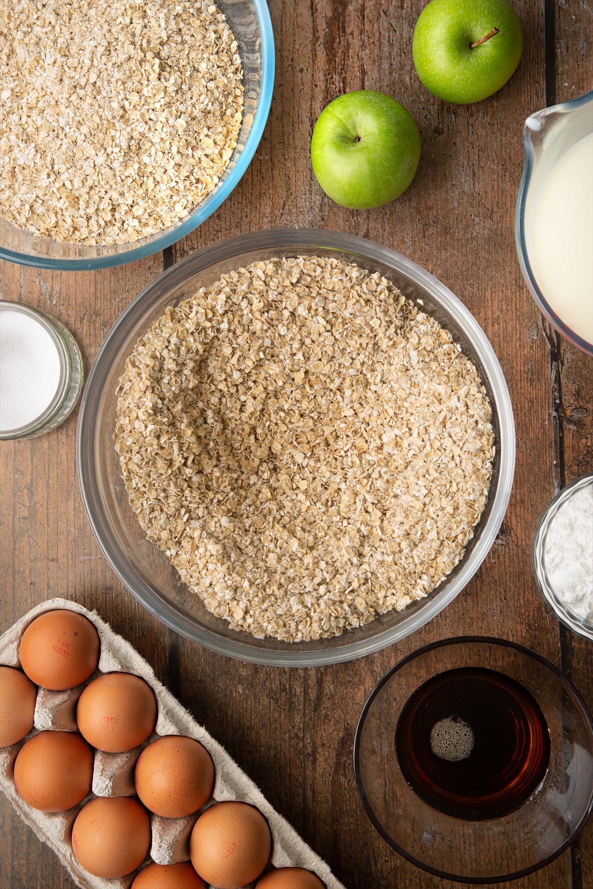 Oats, baking powder and salt whisked together in a glass mixing bowl. Ingredients to make porridge squares surround the bowl.