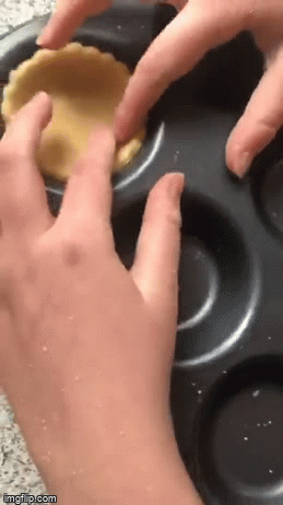 Gif showing a super close up of a child using two hands to press a disk of pastry into a shallow cake tin from the point of view of the child.