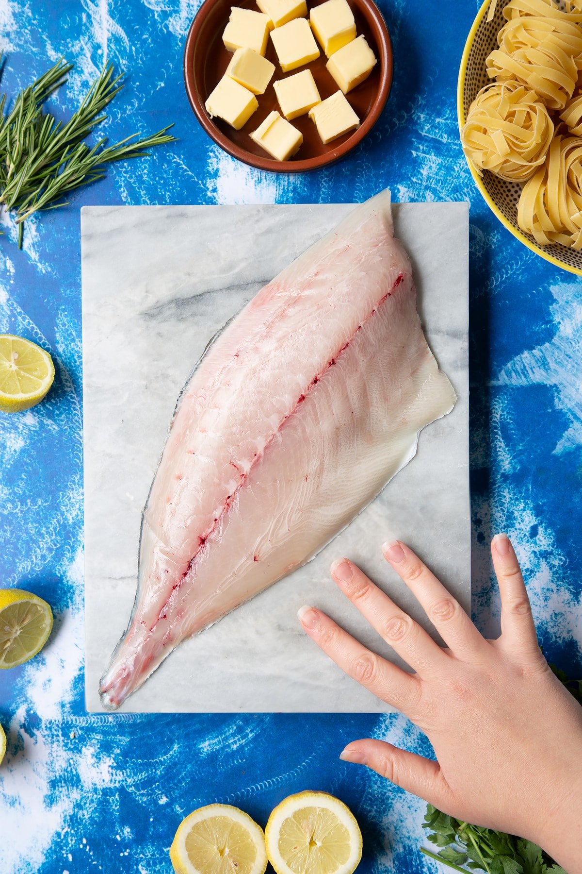 A Dutch Yellowtail fillet on a marble board, skin side down. Hand shown for scale