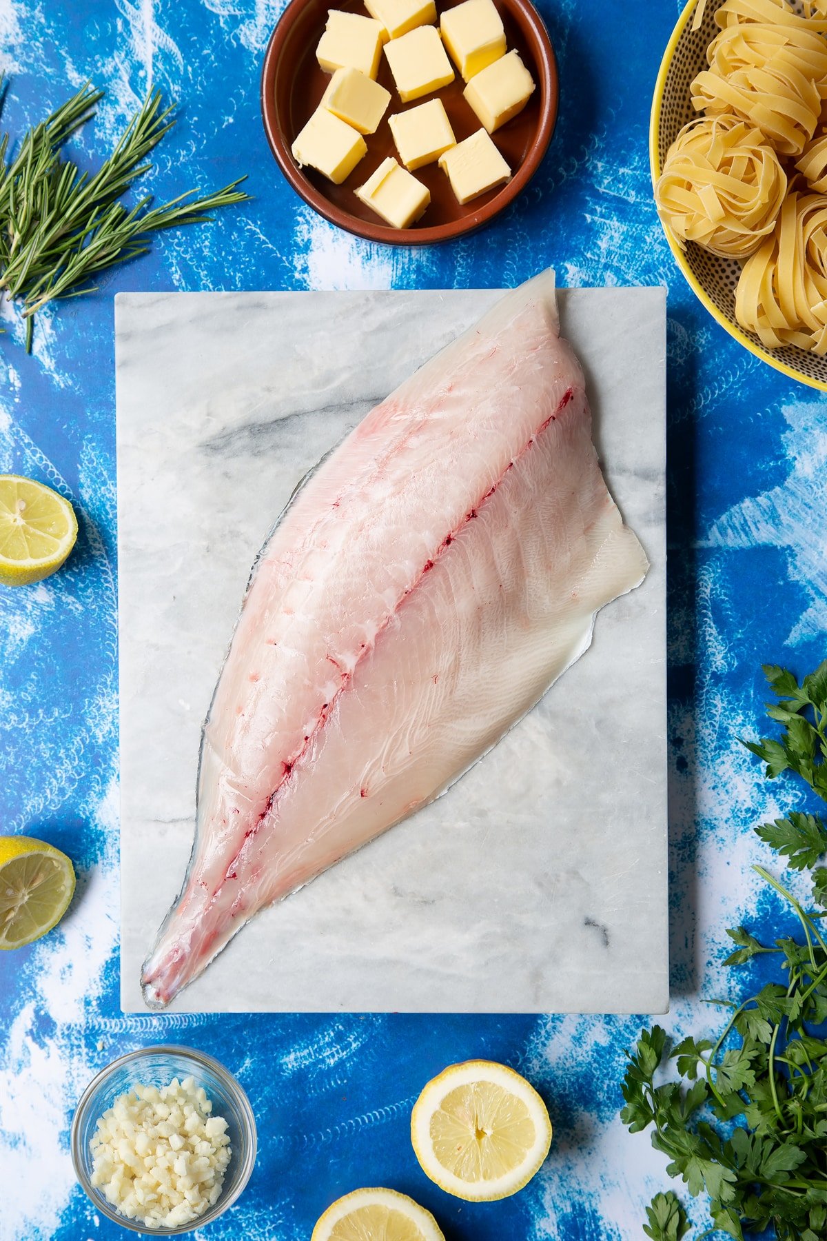 A Dutch Yellowtail fillet on a marble board, skin side down. Hand shown for scale