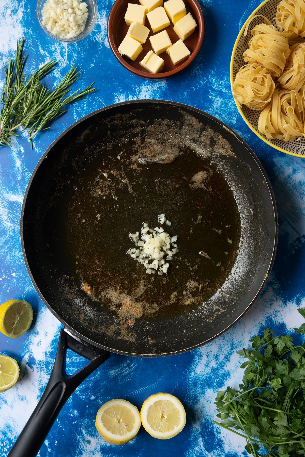 A large frying pan with melted butter and fresh chopped garlic. Ingredients to make Dutch Yellowtail tagliatelle surround the pan.