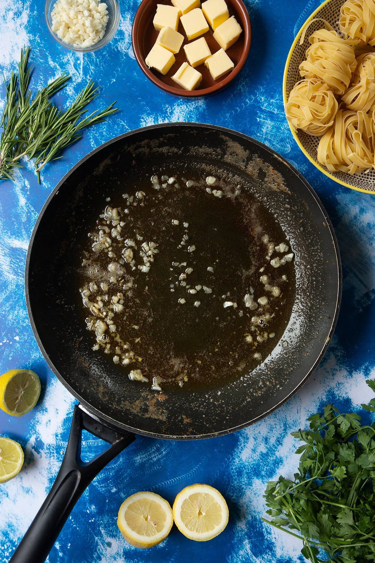 A large frying pan with melted butter and garlic. Ingredients to make Dutch Yellowtail tagliatelle surround the pan.