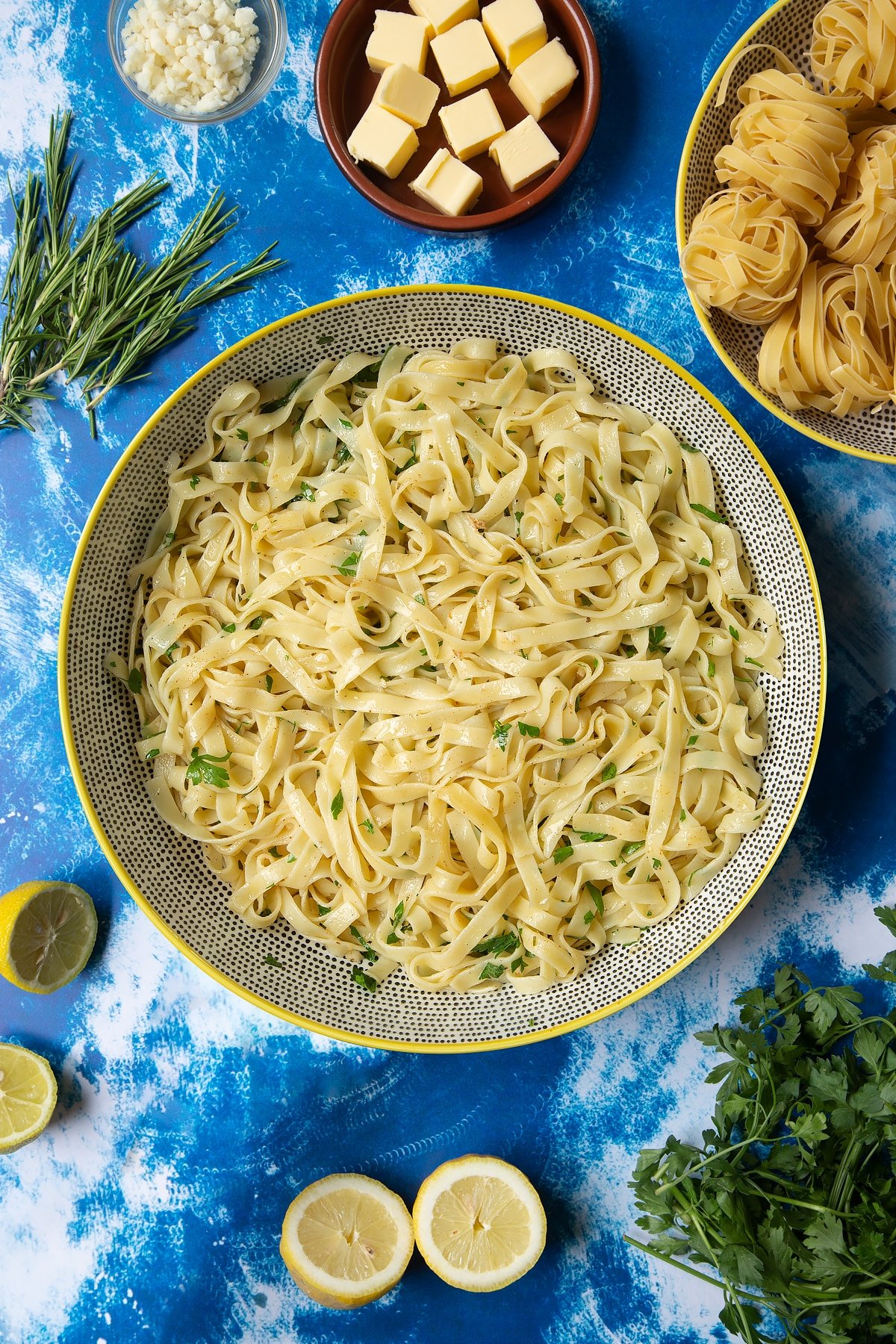 A large bowl with tagliatelle, rosemary and parsley. Ingredients to make Dutch Yellowtail tagliatelle surround the bowl.