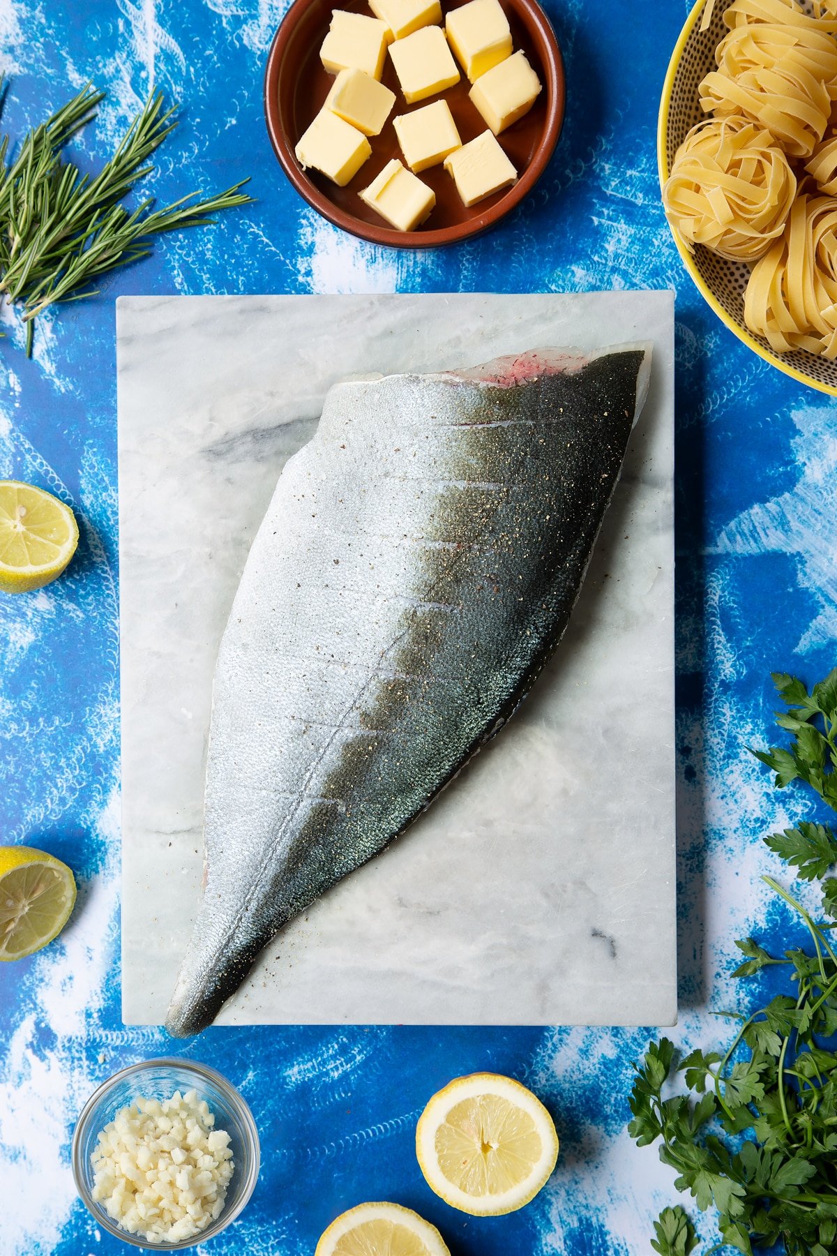 A Dutch Yellowtail fillet on a marble board, skin side up. The fish is seasoned with salt and pepper and the skin in scored.