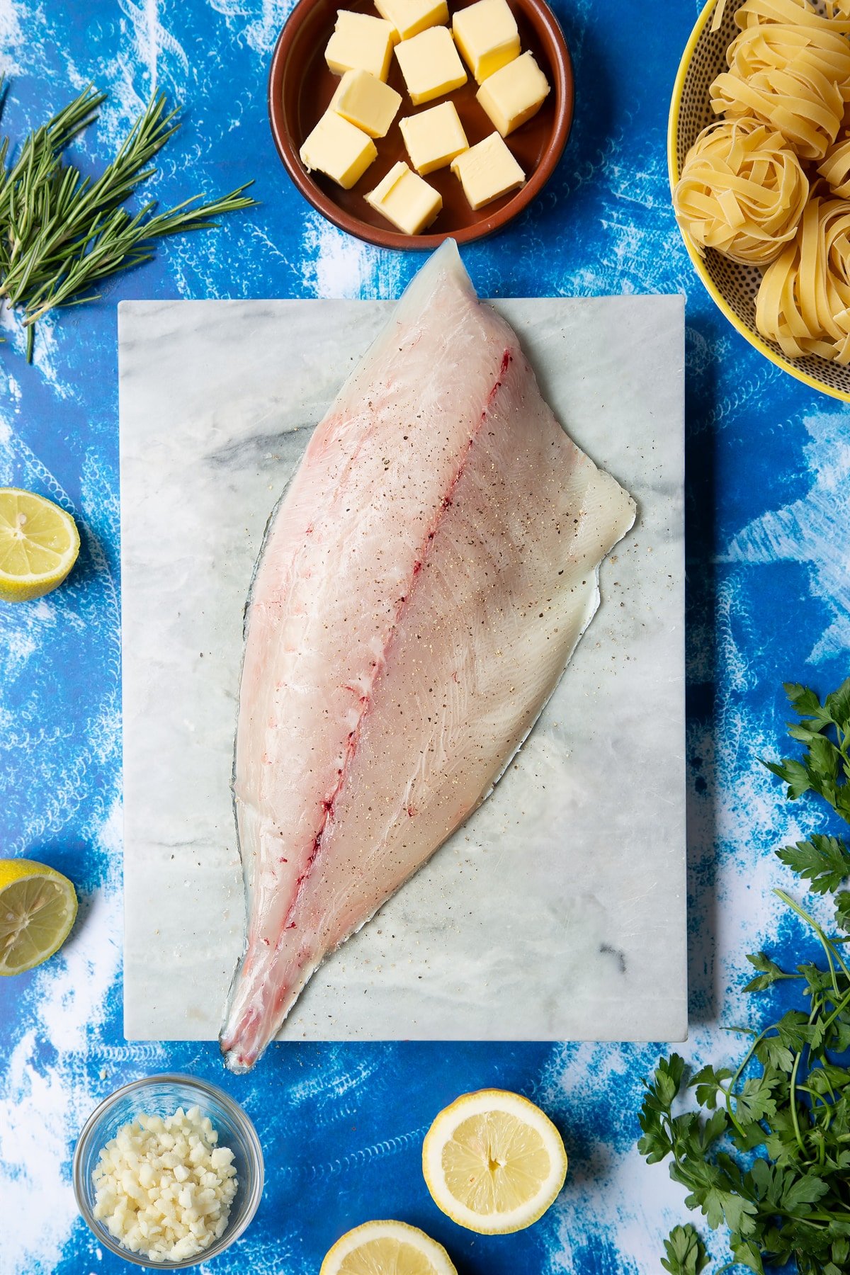 A Dutch Yellowtail fillet on a marble board, skin side down, seasoned with salt and pepper. Hand shown for scale