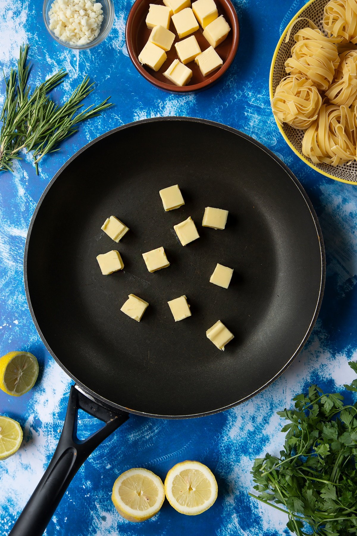 A large frying pan with cubes of butter. Ingredients to make Dutch Yellowtail tagliatelle surround the pan.