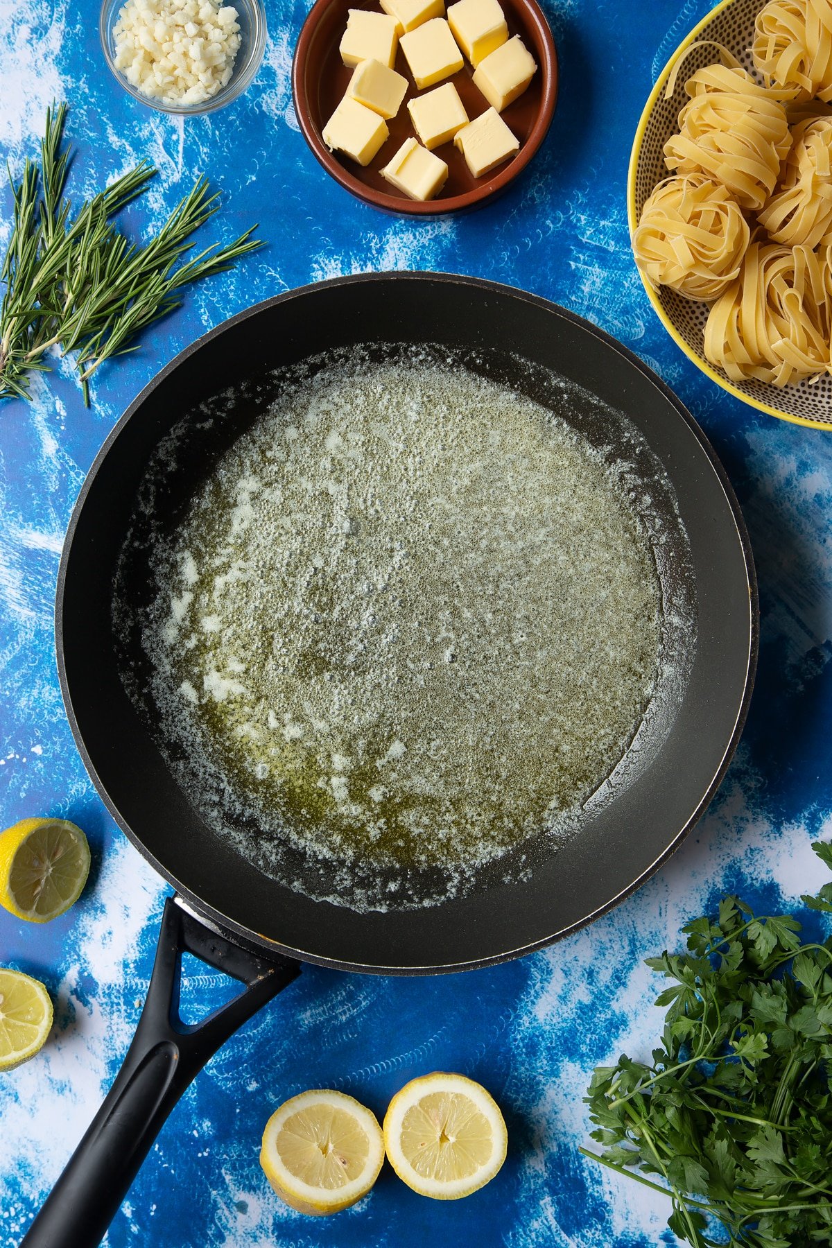 A large frying pan with melted butter. Ingredients to make Dutch Yellowtail tagliatelle surround the pan.